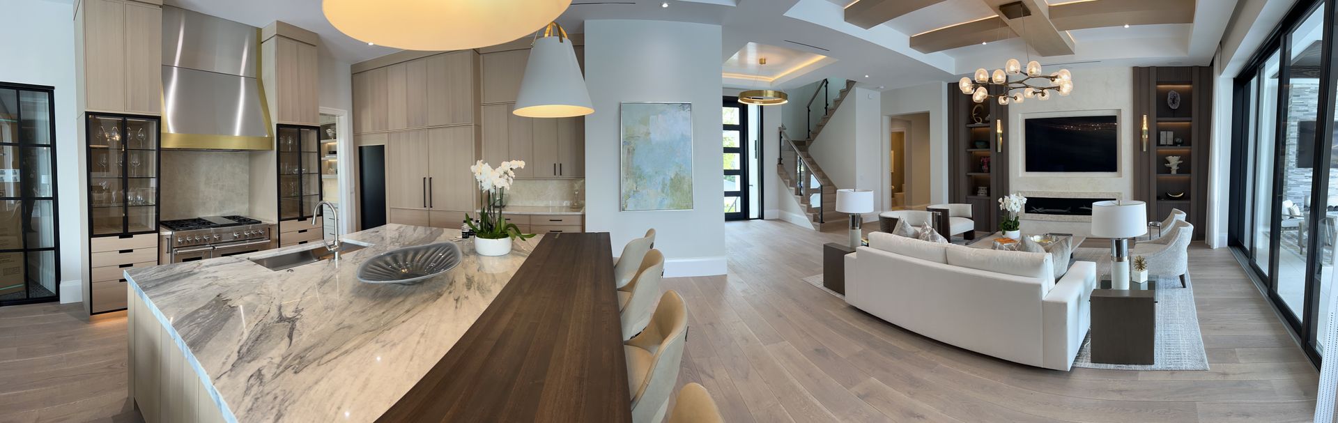 Spacious modern kitchen and living area with light wood floors, white walls, and a large island.