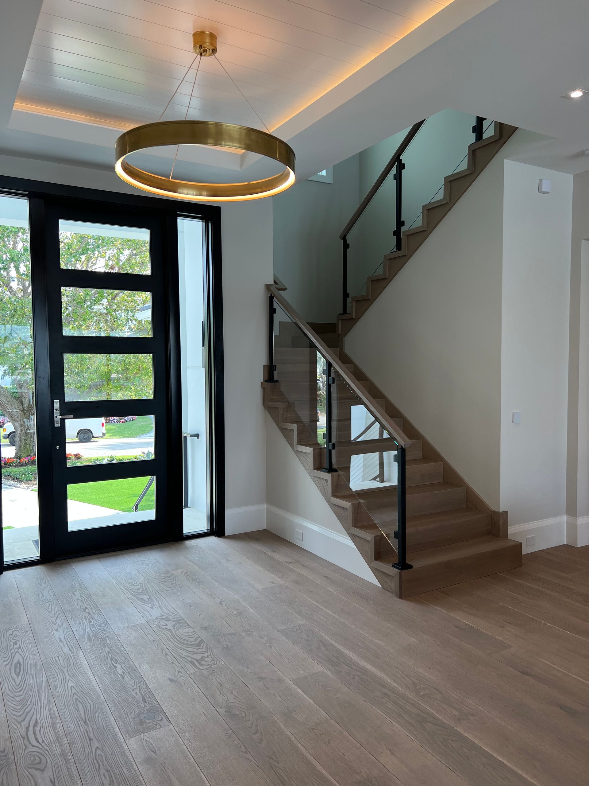 Entryway with a modern staircase, hardwood floors, and a gold ring light fixture.