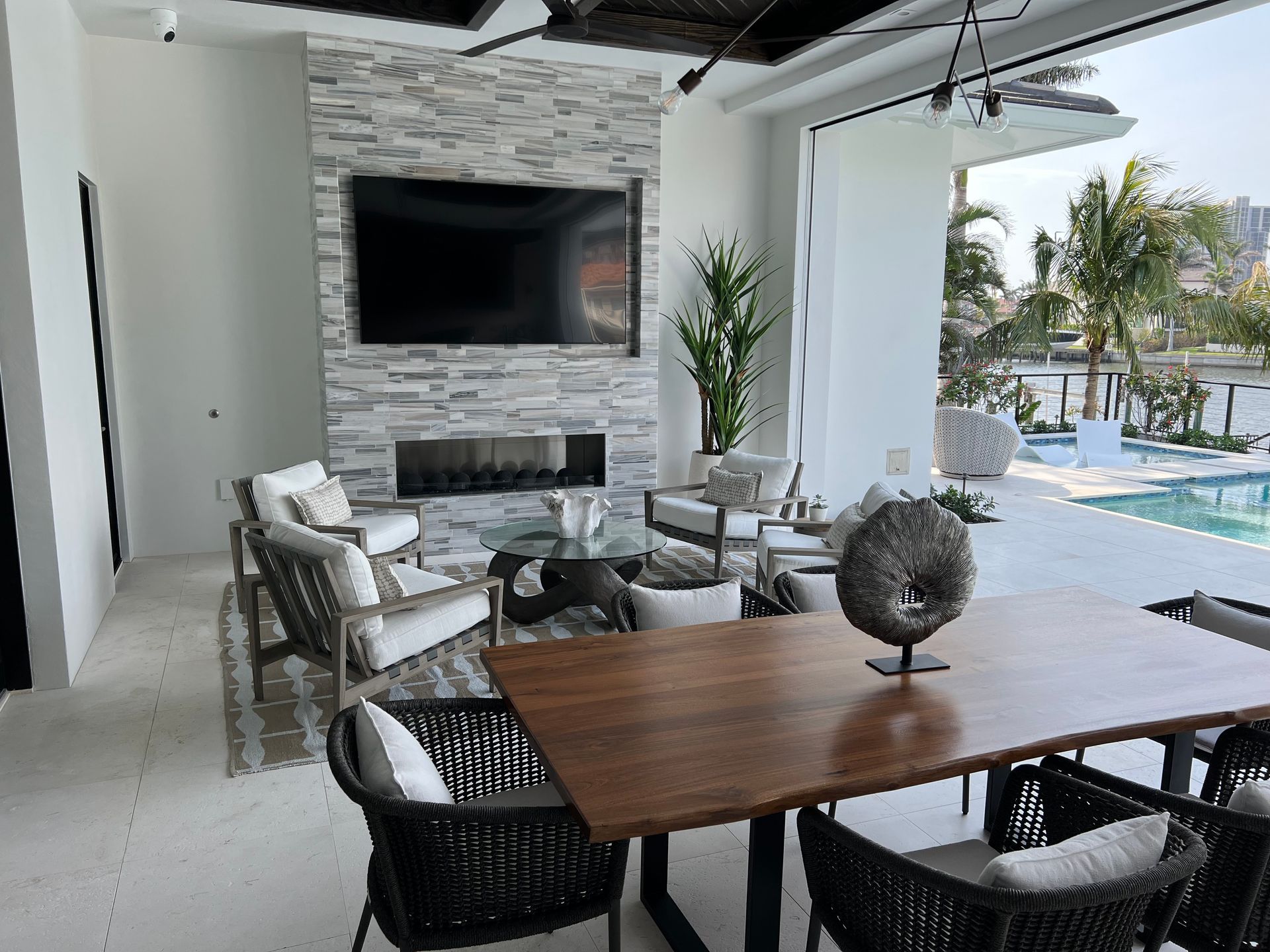 Living room with stone fireplace, TV, seating area, and dining table overlooking a pool.