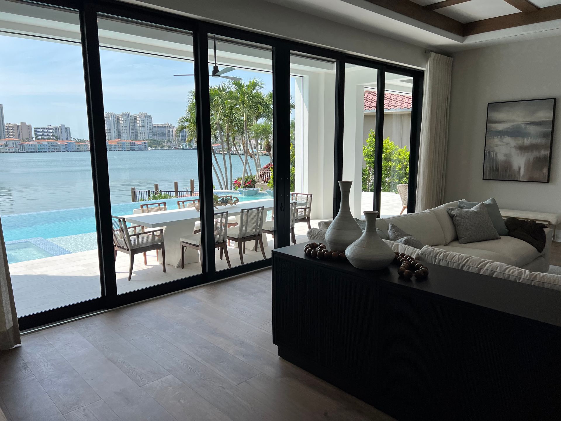 Living room with waterfront view; open doors to patio, pool, and city.