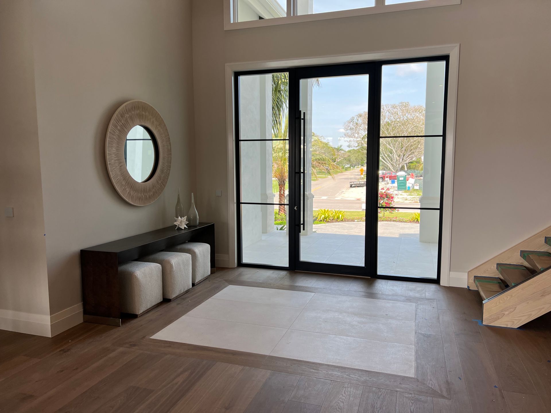 Entryway with black framed glass doors, light wood floors, neutral walls, and a bench with ottomans.