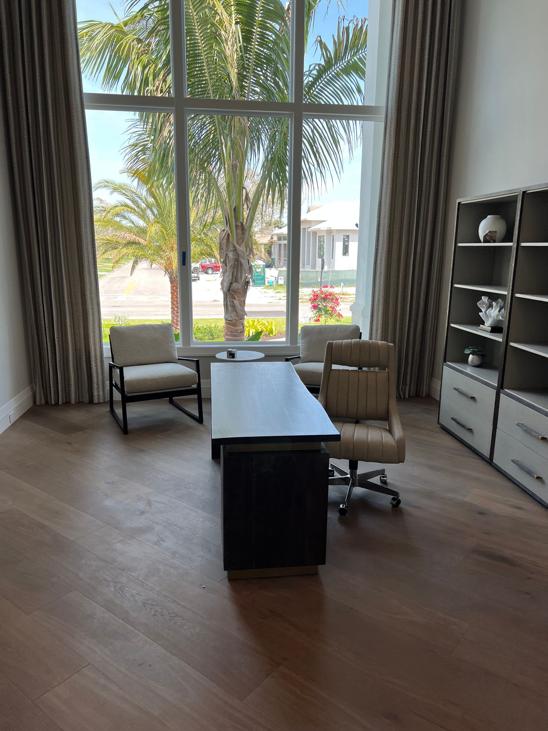 Office with large windows, desk, chairs, and bookshelves; neutral colors.