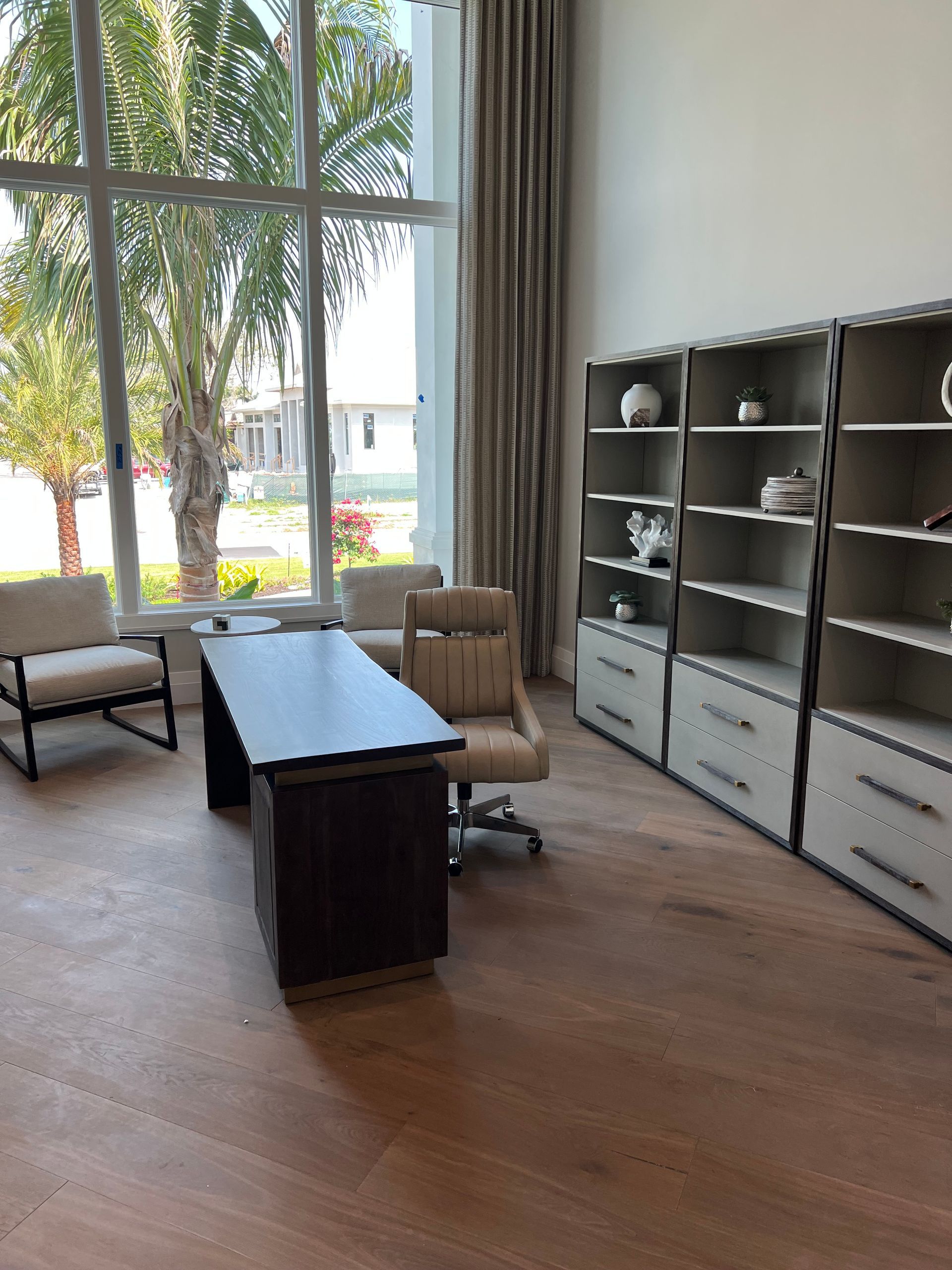 Office with desk, chair, bookcases, and large window overlooking palm trees.