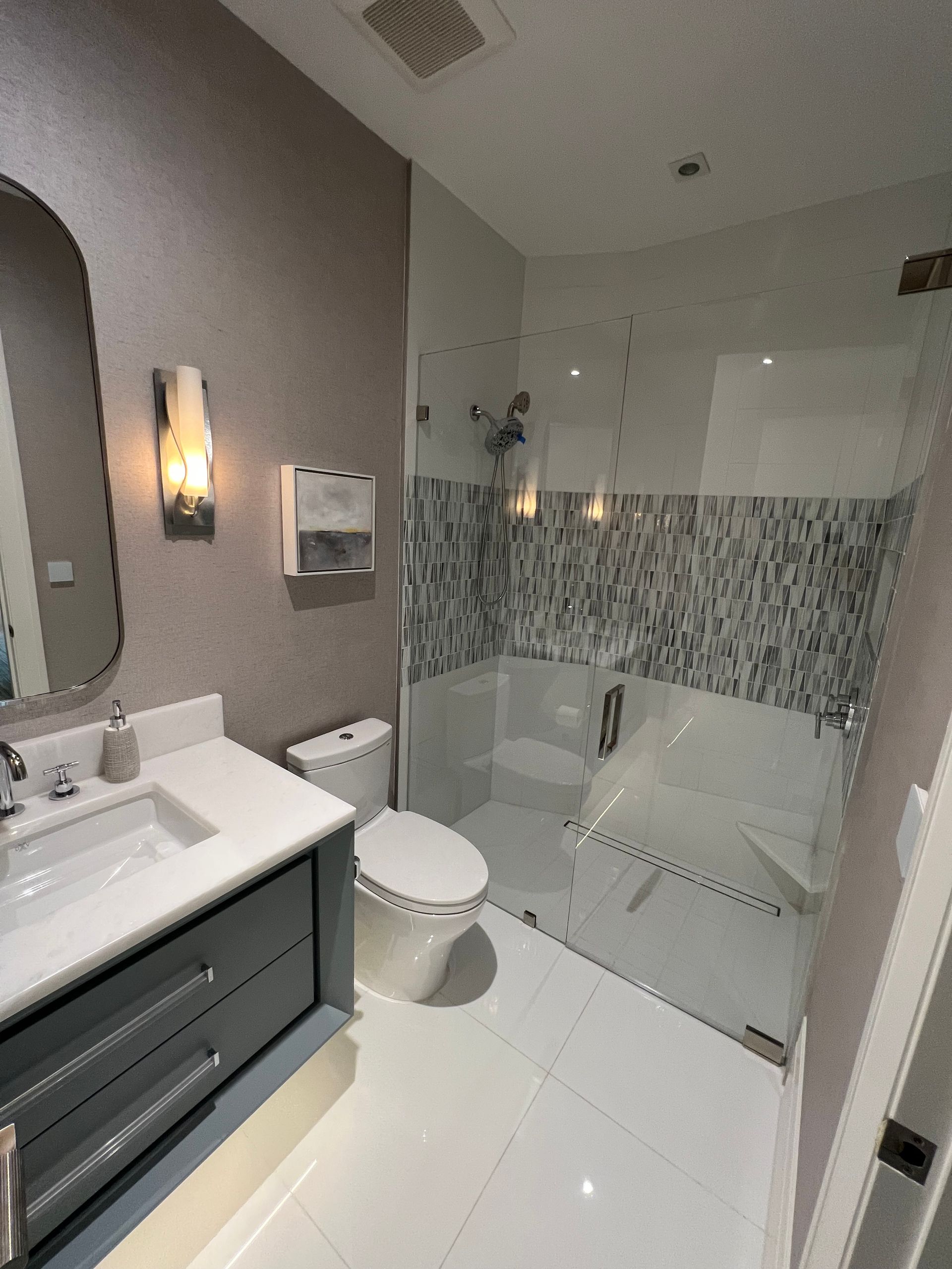 Bathroom with white tiles, glass shower, gray vanity, and neutral walls.