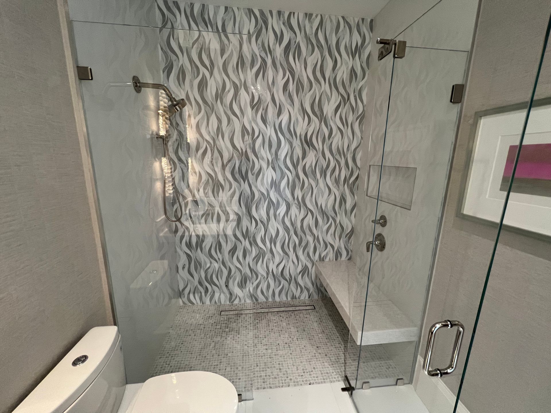 Modern bathroom with glass shower, patterned tile wall, bench, and toilet.