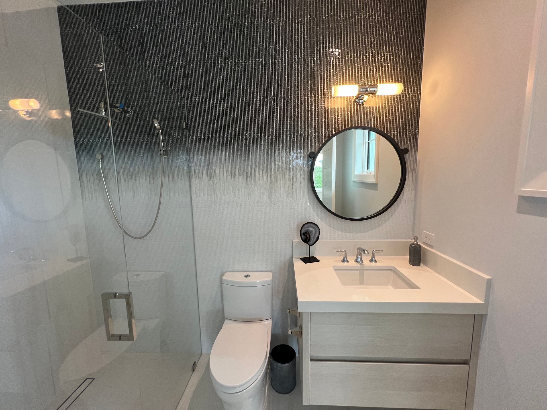 Modern bathroom with a glass shower, toilet, vanity, and a decorative black and white wall.