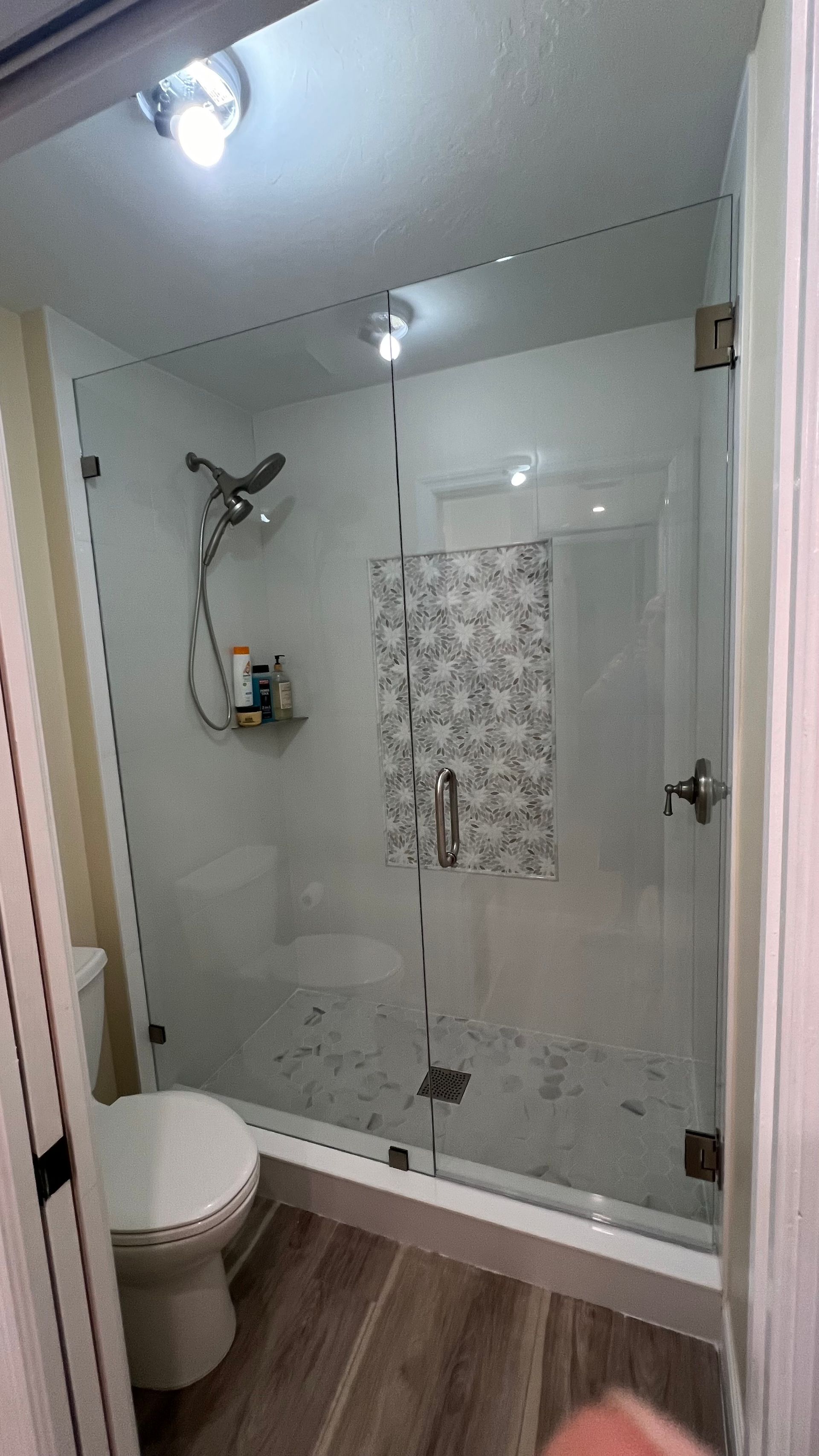 Glass shower with gray and white tile, silver fixtures, and a toilet in a bathroom.