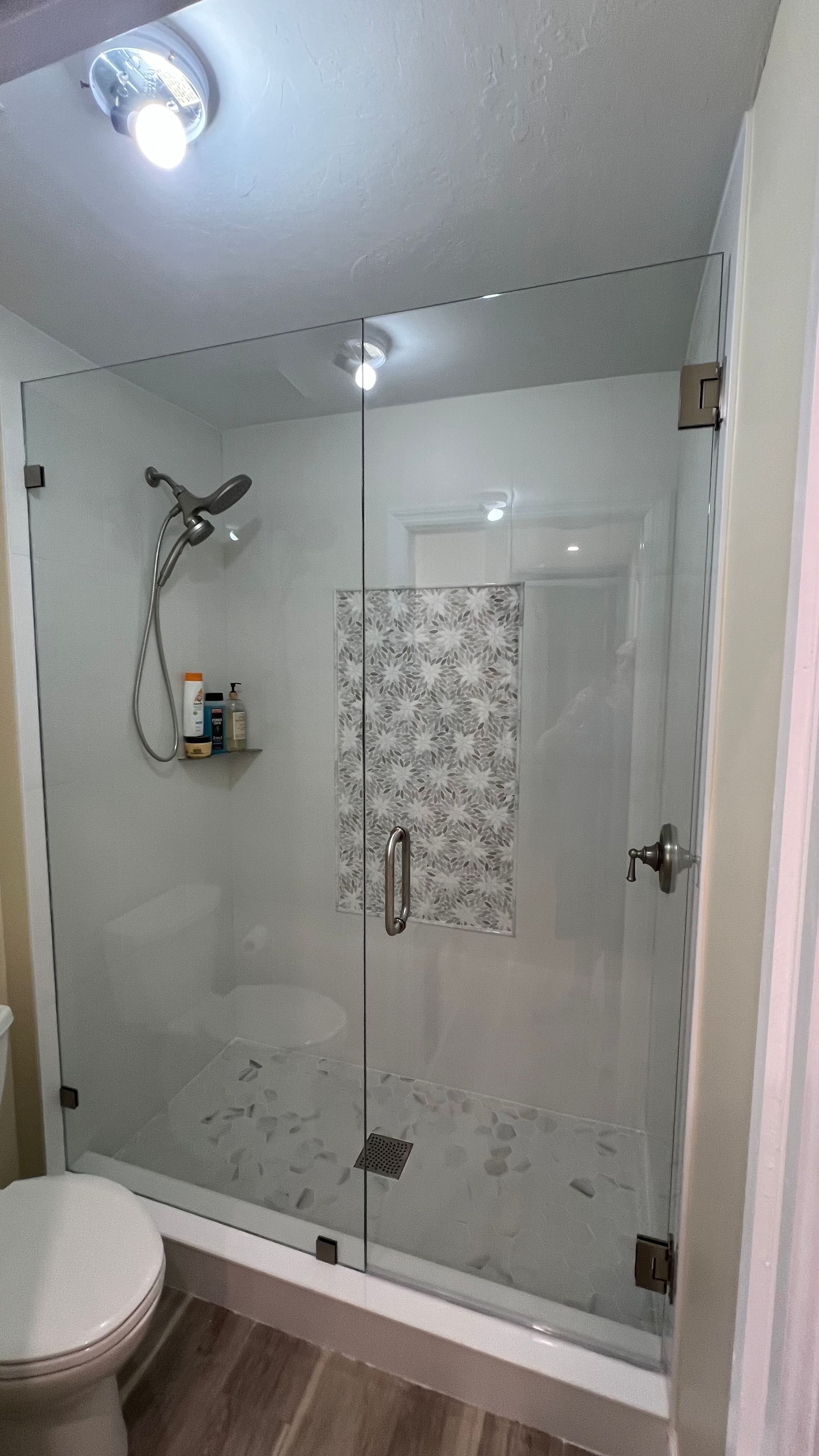 Shower with glass doors, gray and white tile, chrome fixtures, toilet in the foreground, recessed lighting.
