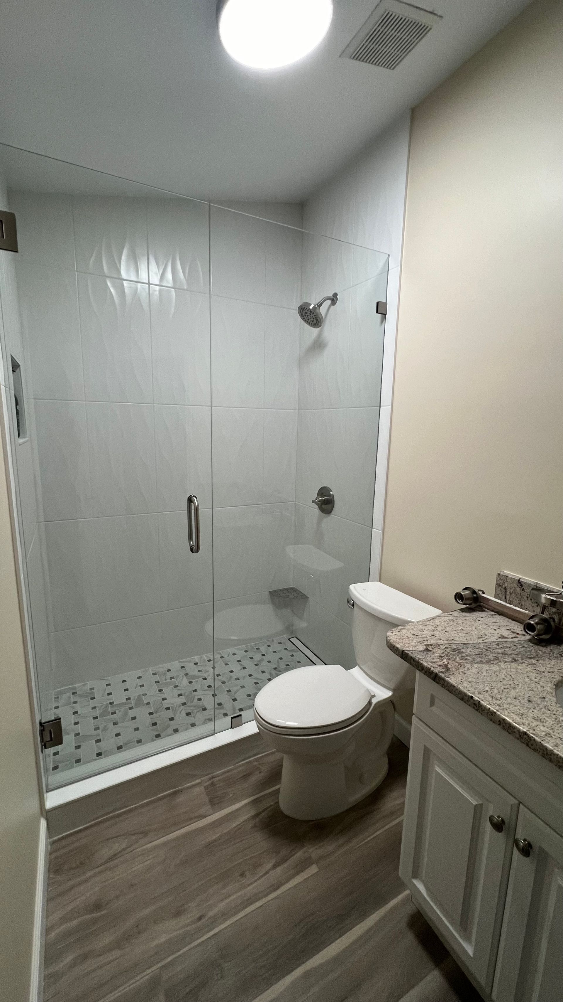 Bathroom with a glass shower, white subway tile, toilet, and vanity with granite countertop.