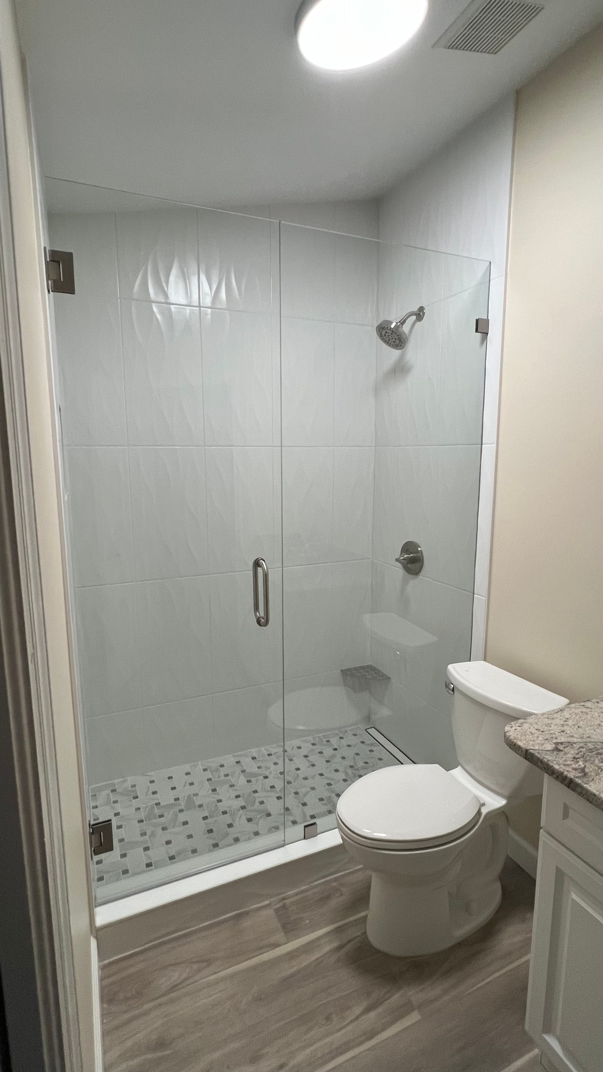 Modern bathroom with a glass shower, toilet, and light-colored tiled floor and walls.