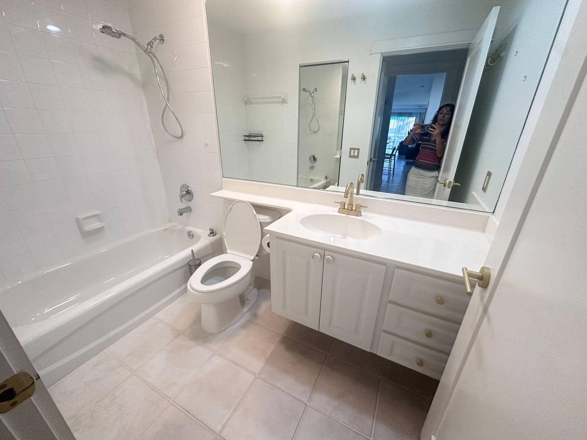 White bathroom with tub, toilet, vanity, and large mirror. Person reflected in mirror.