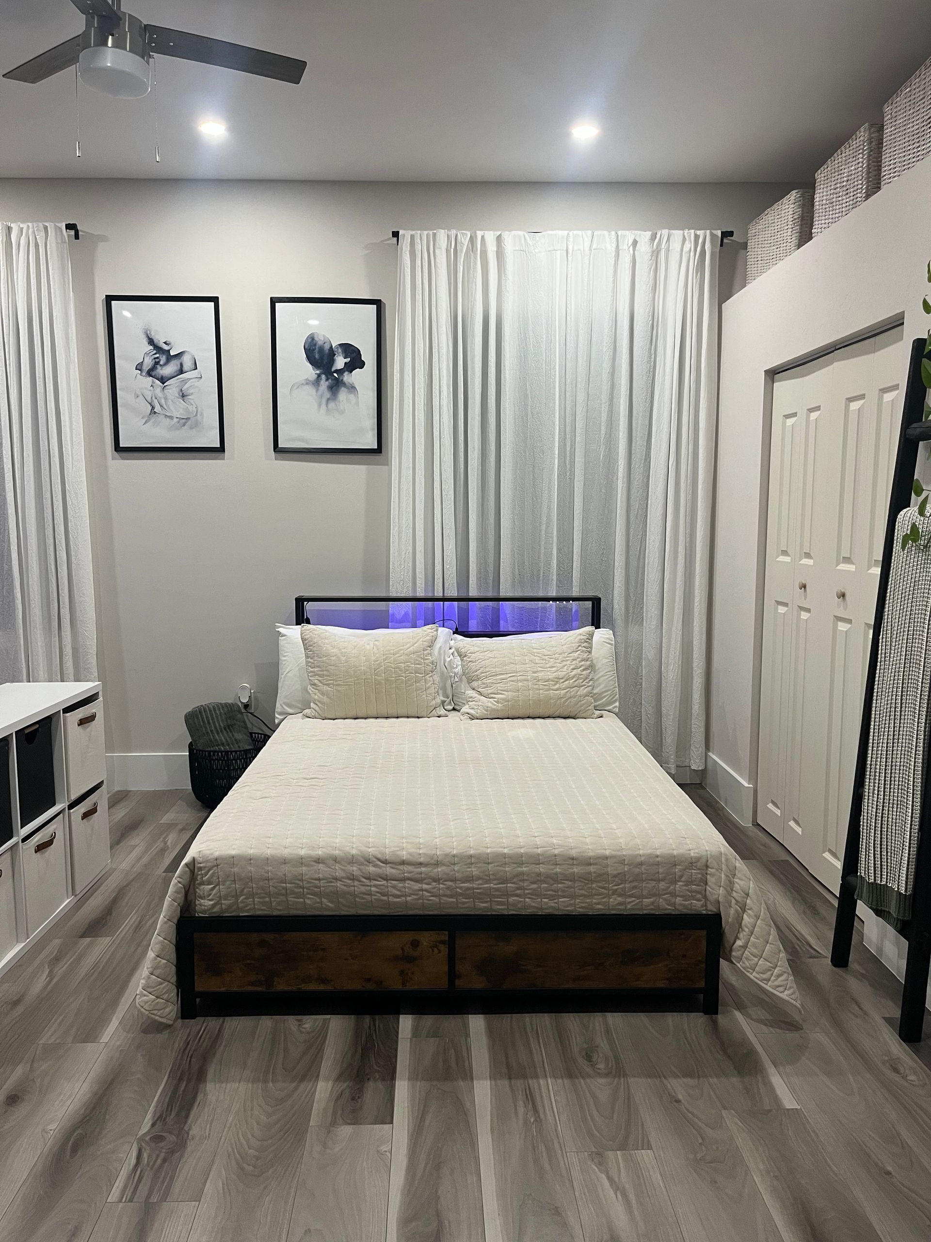 Bedroom with a bed, artwork, and closet; gray walls, light-colored flooring and curtains.