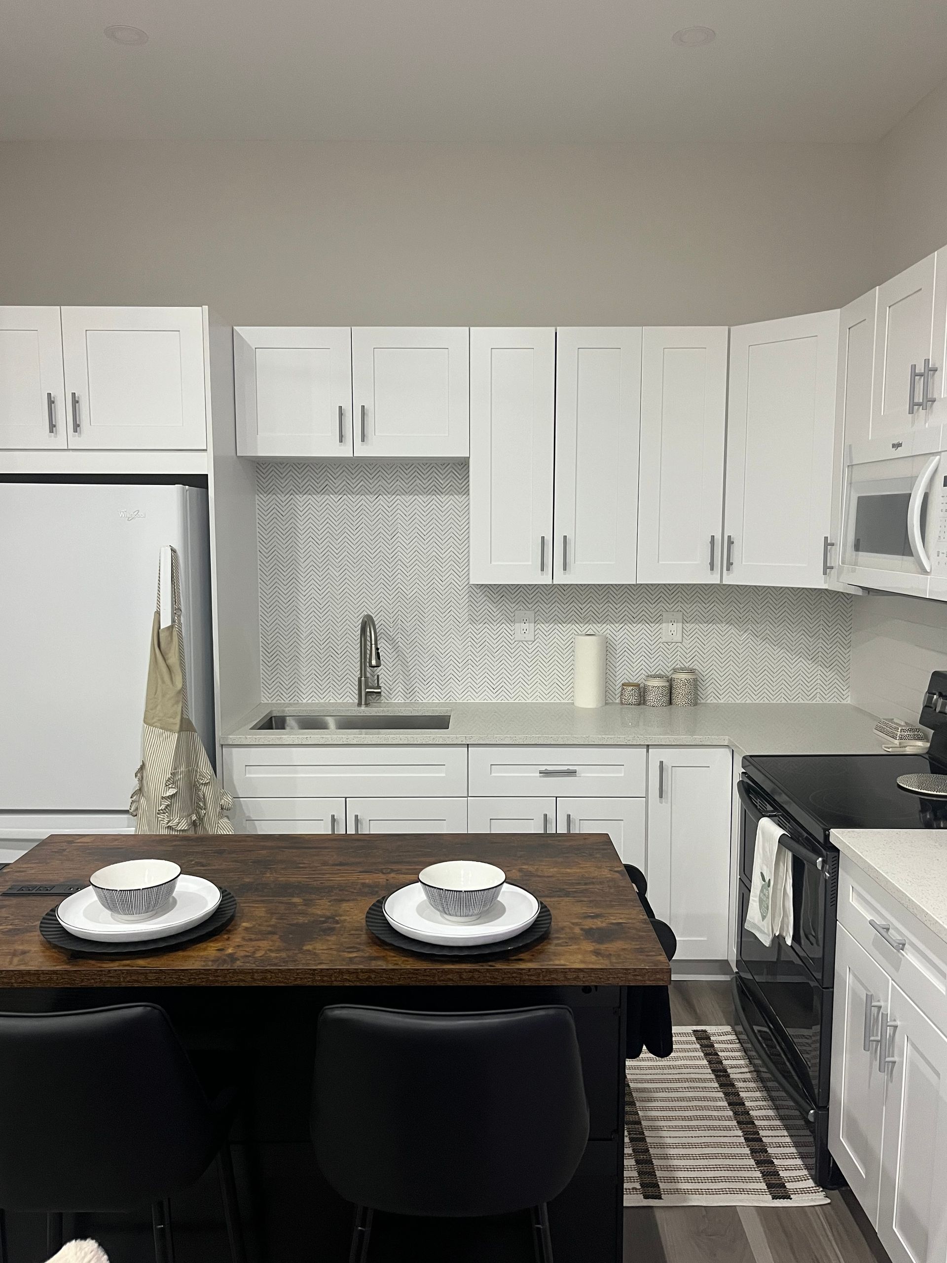 Modern white kitchen with dark island, stainless steel appliances, and patterned backsplash.