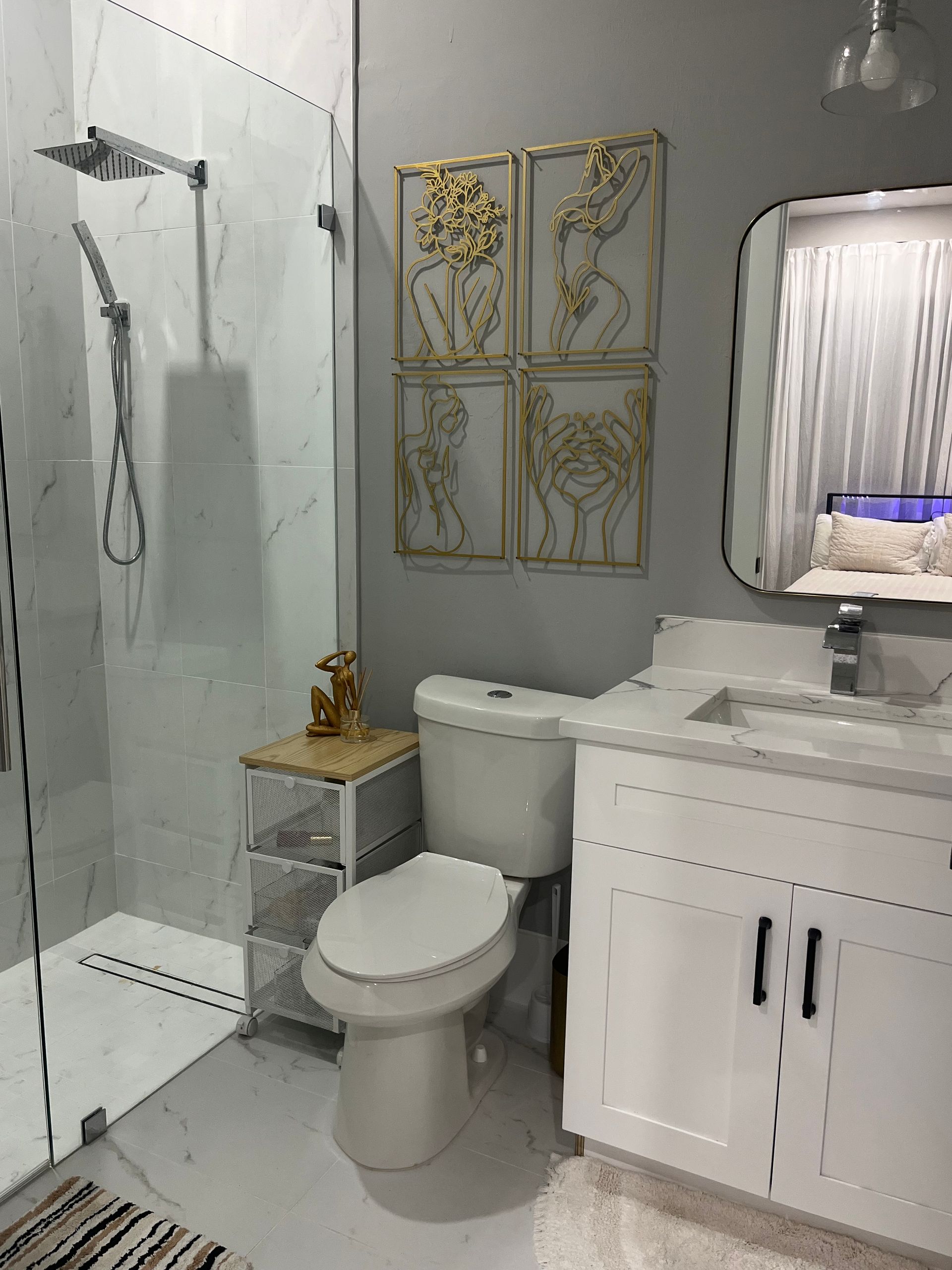 Modern bathroom with a glass shower, white vanity, toilet, and gold wall art.