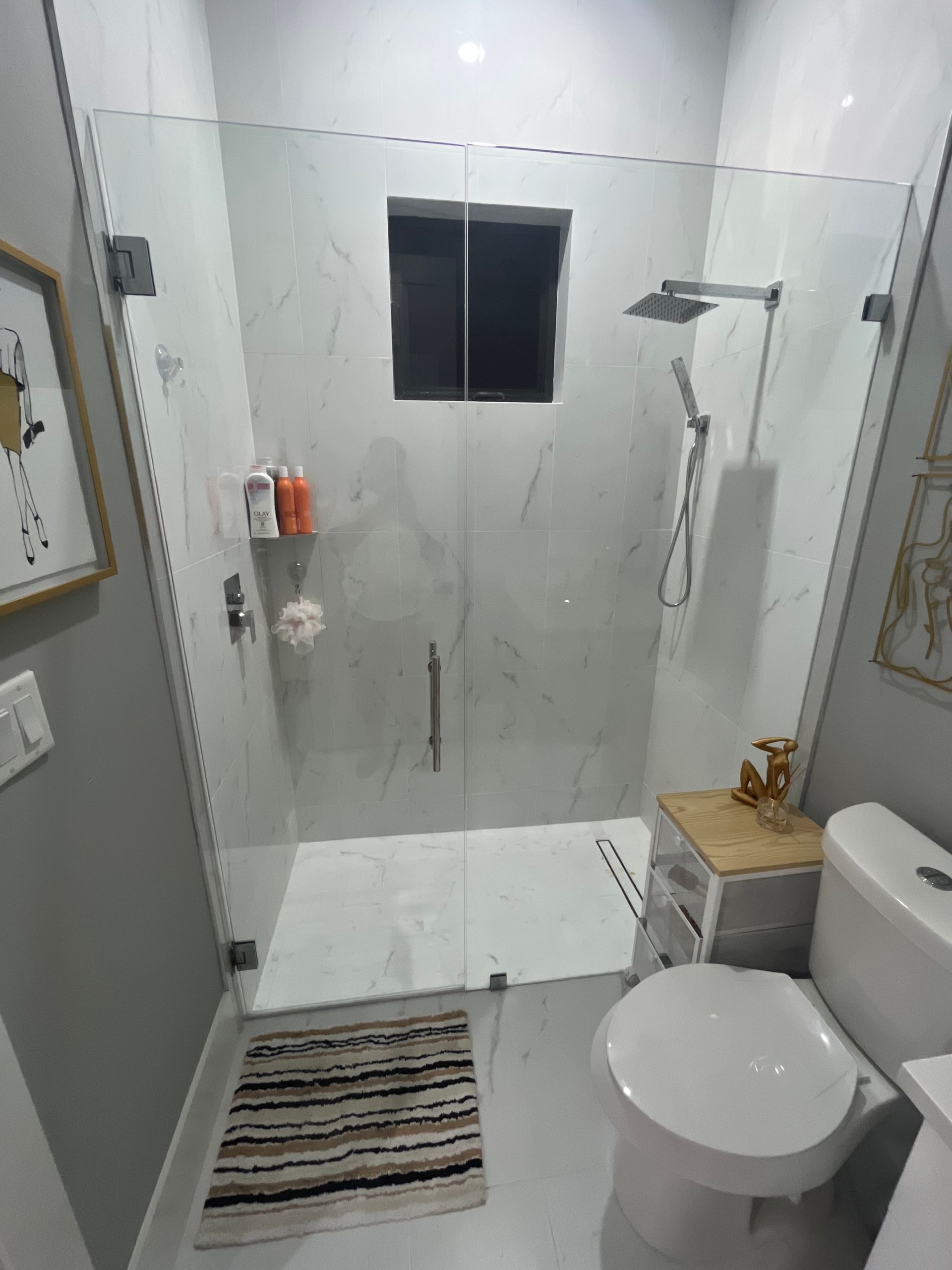 Modern bathroom with a glass shower, marble tiles, and a toilet.