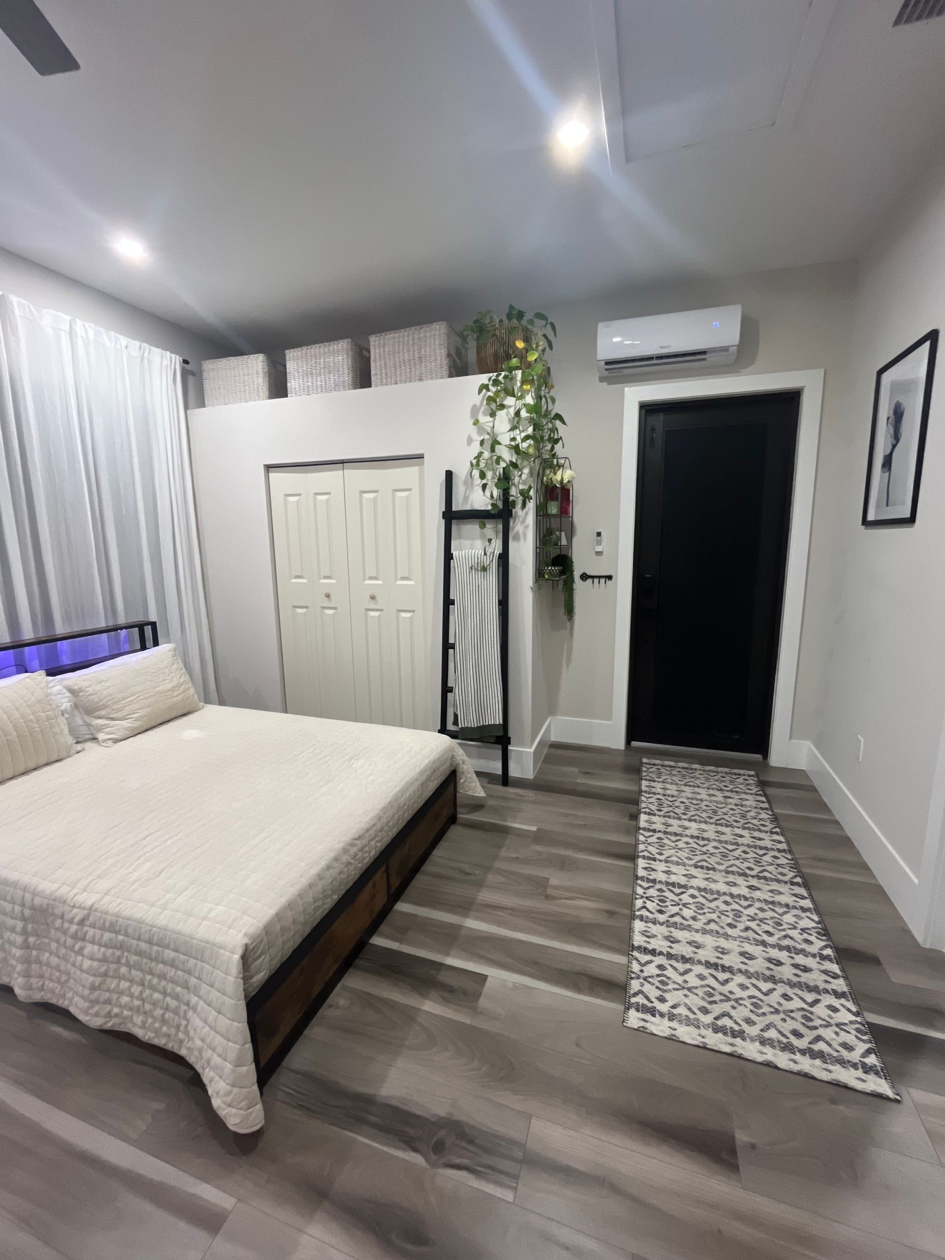 Bedroom with a bed, black door, and a decorative plant.