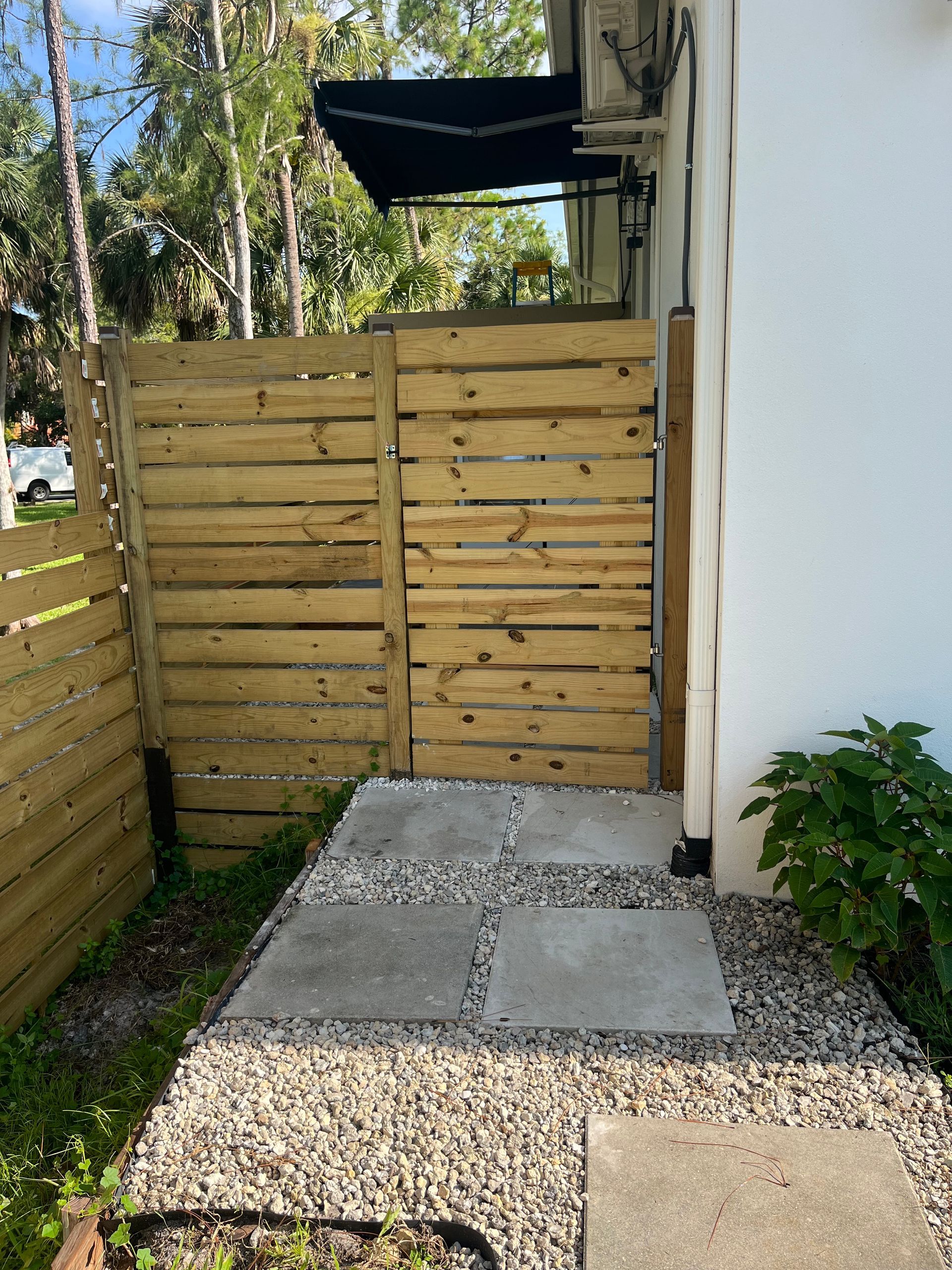 A wooden fence and gate leading to a walkway with stepping stones. A white building is on the right.