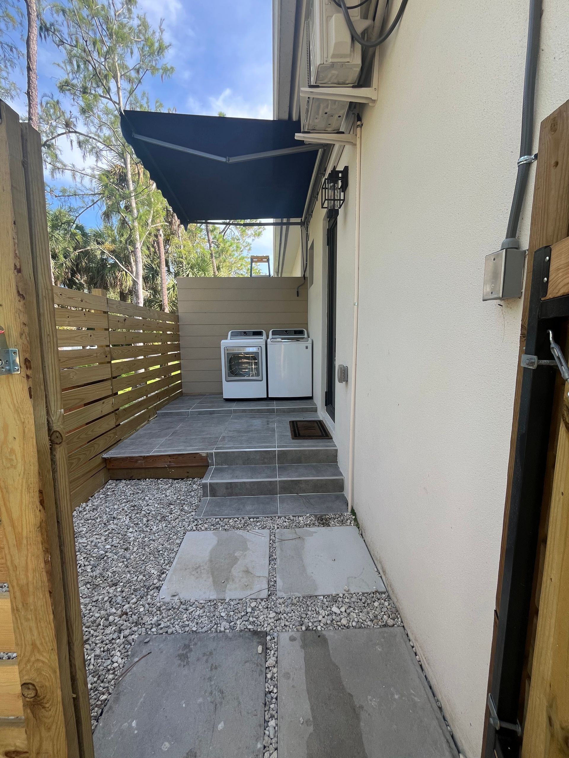 Backyard with washer, dryer under awning; stone path and wooden fence visible.