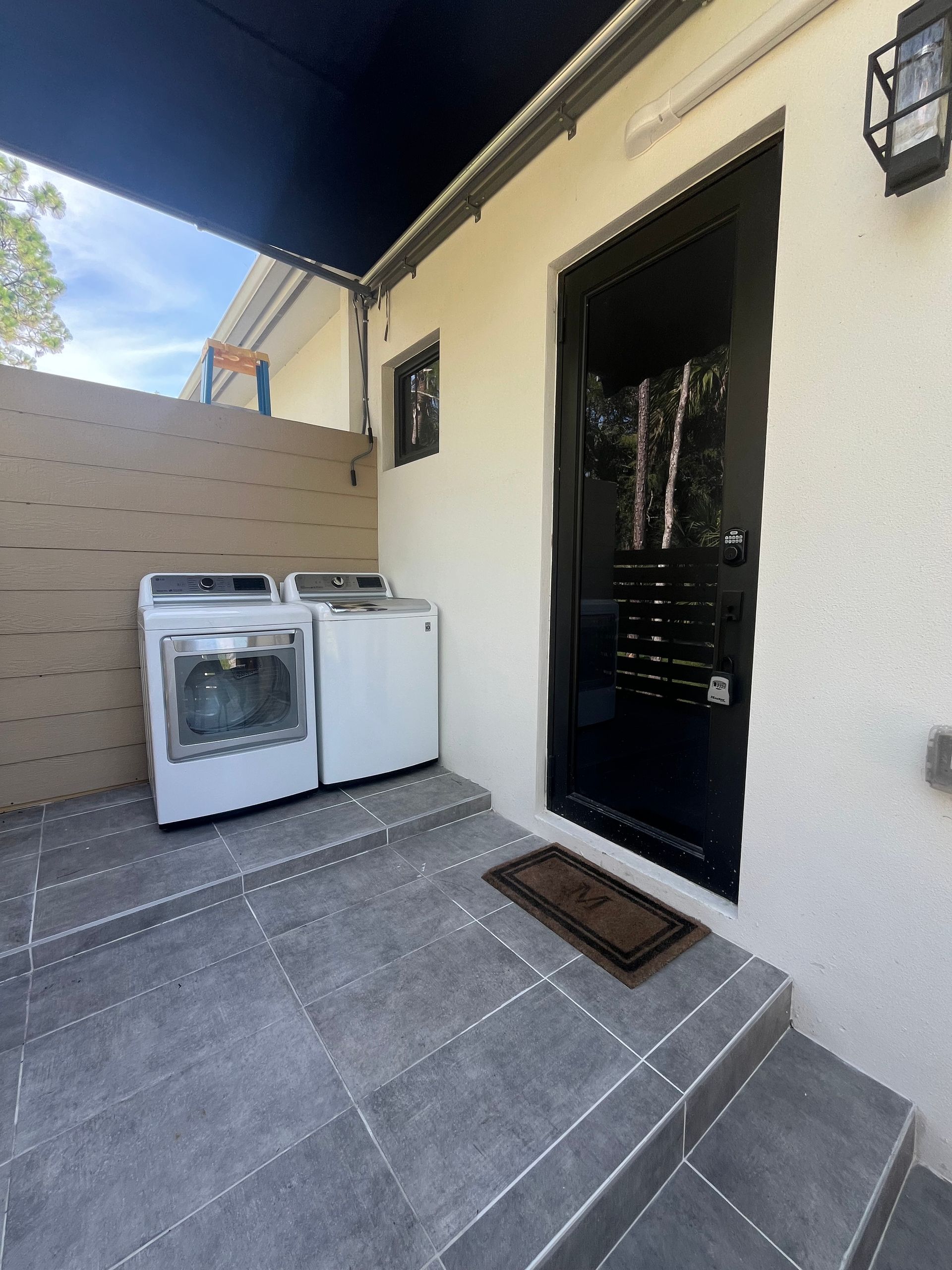 Laundry area with washing machine and dryer, black door, and outdoor steps.