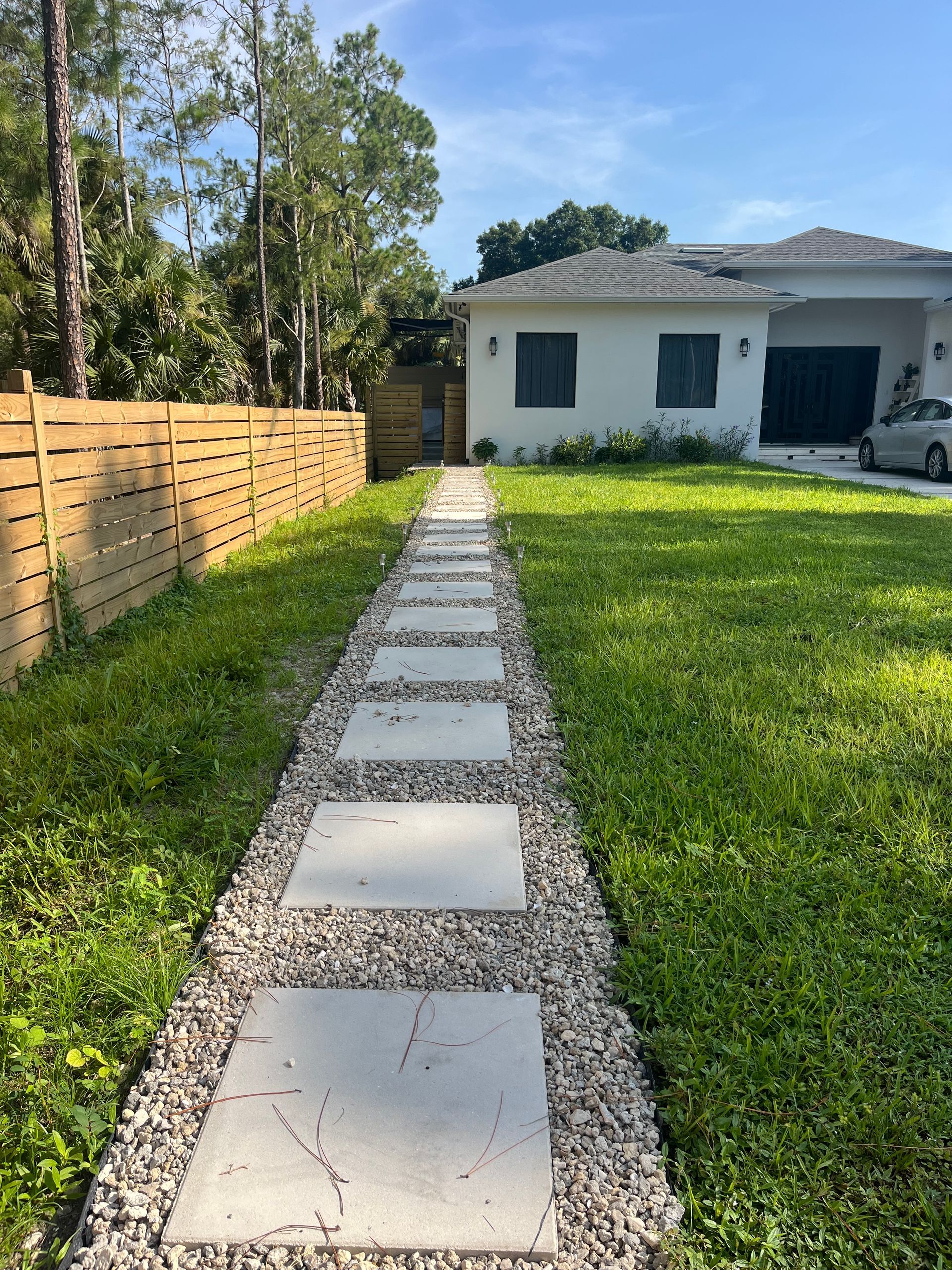 Stone path leading to a white house with a green lawn and wooden fence.