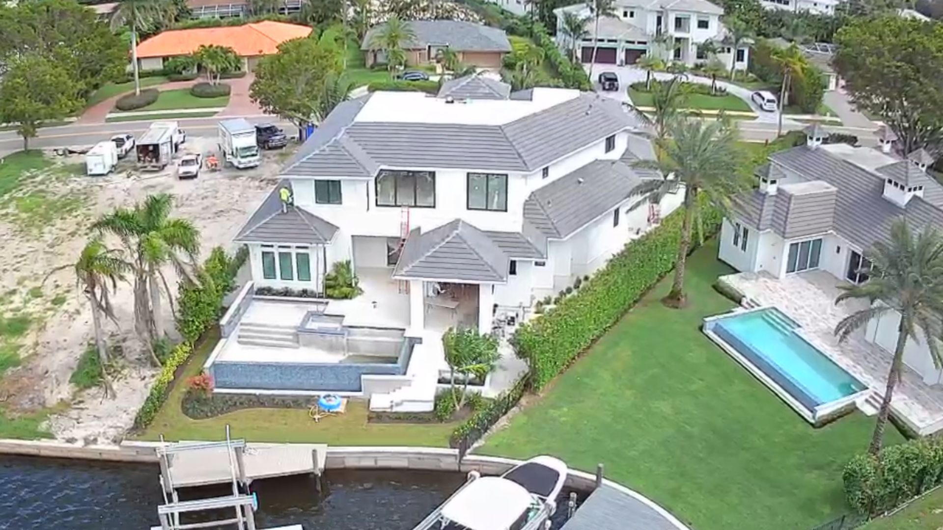 Aerial view of a large white house with a pool, dock, and grassy yard on a waterfront.