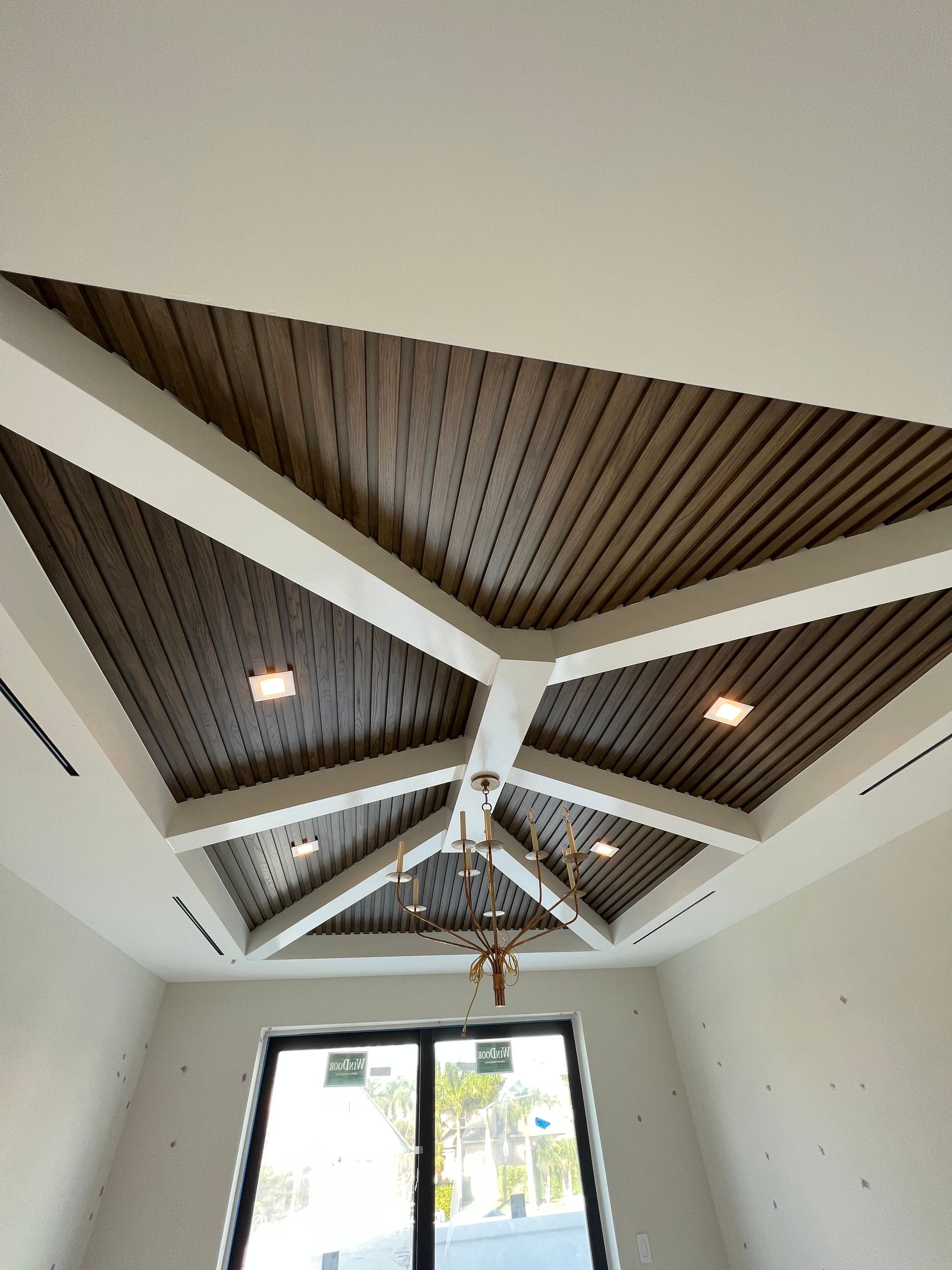 White and brown wooden ceiling with beams, recessed lights, and a chandelier.