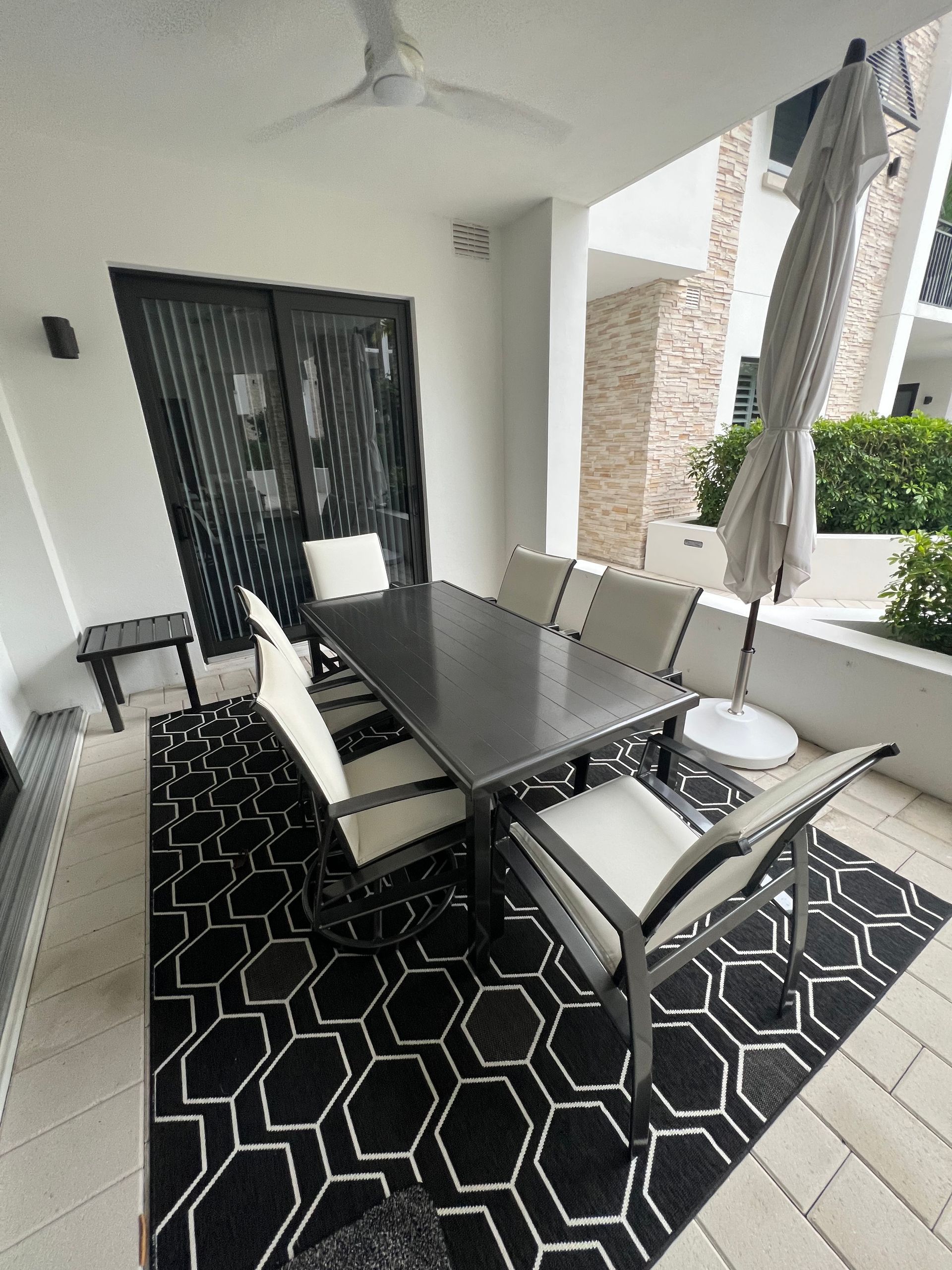 Outdoor patio with a table and chairs on a black and white rug, umbrella, and sliding doors.
