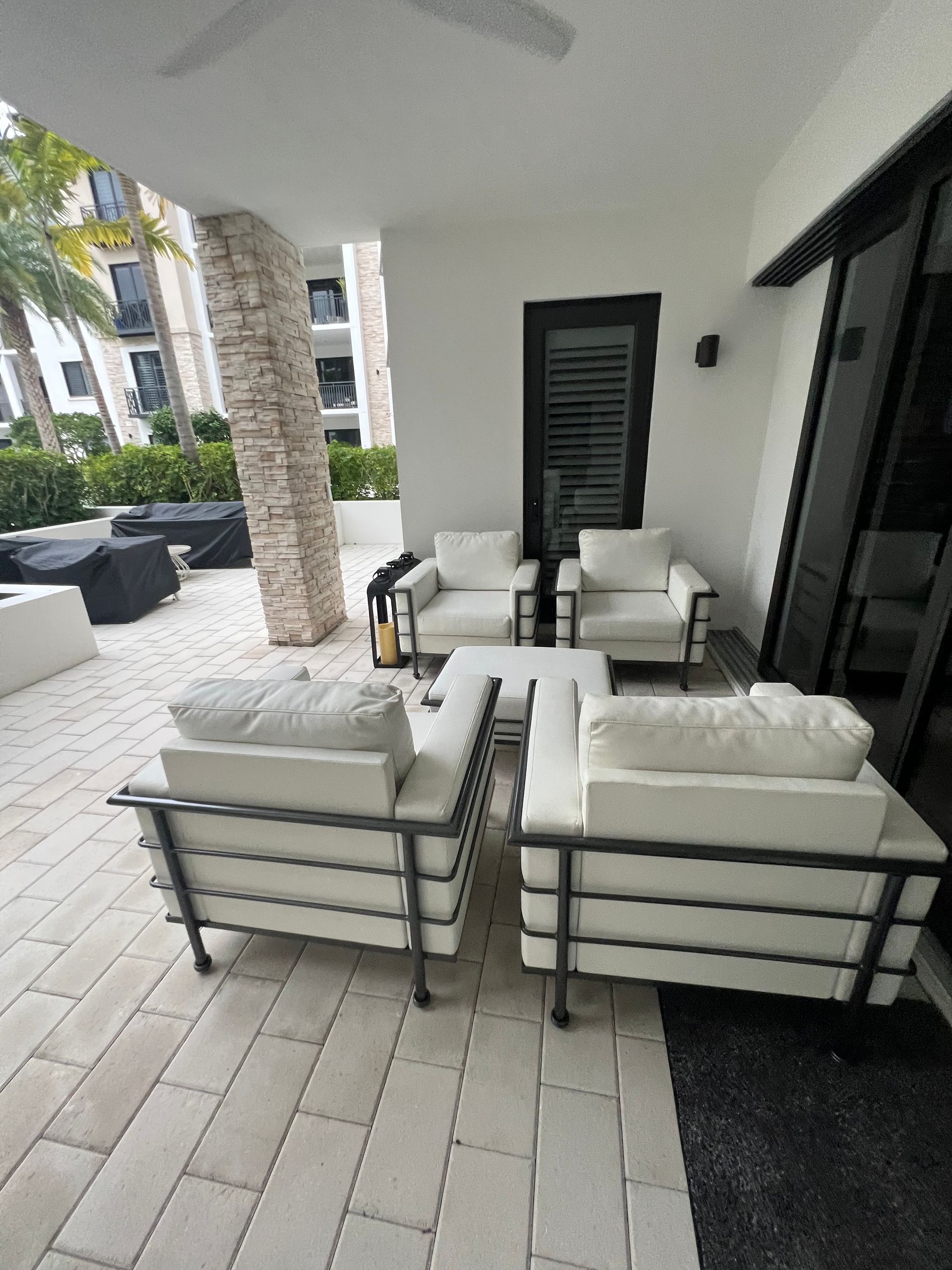 Outdoor patio with white furniture, stone flooring, and a view of a building.