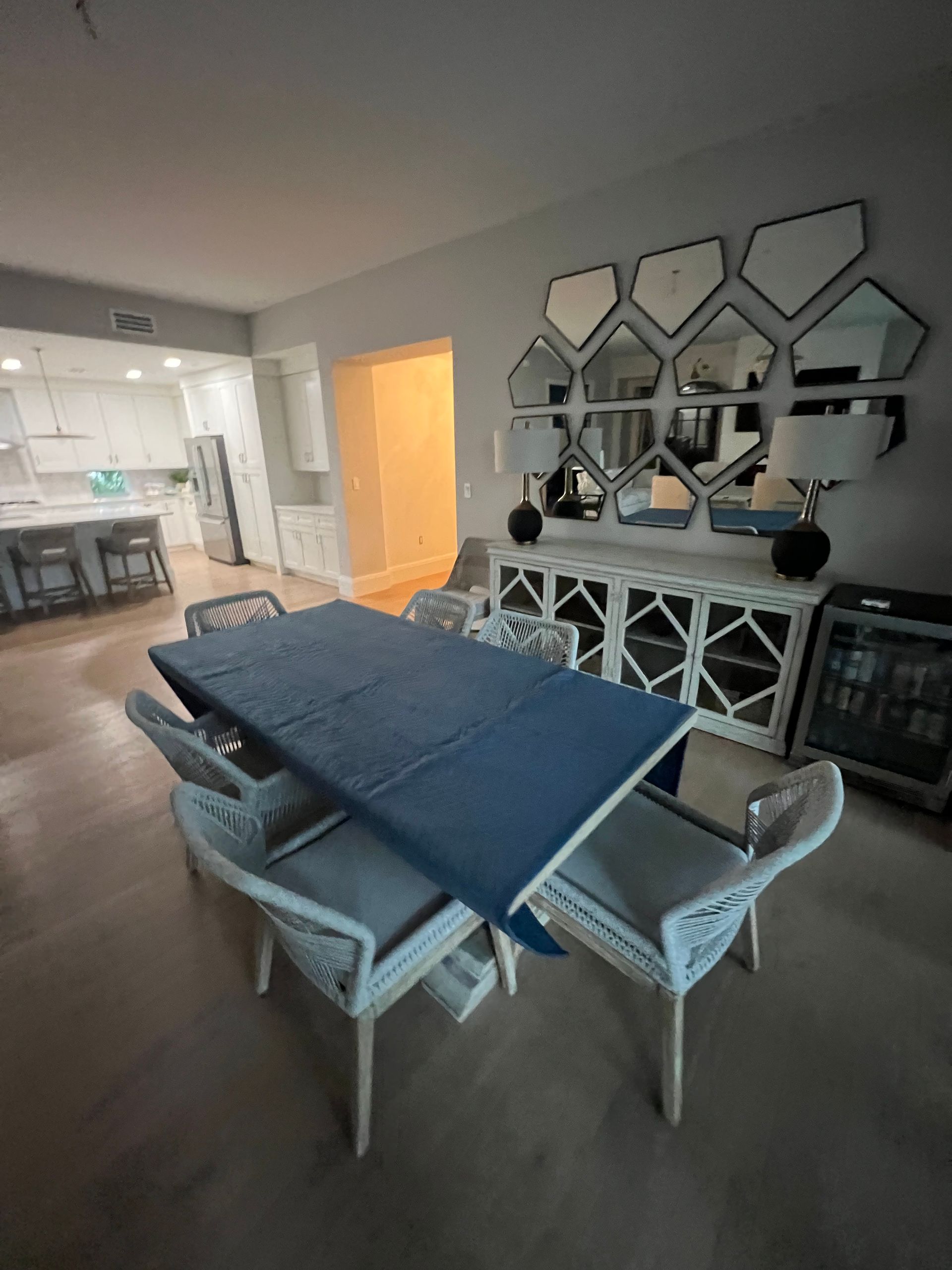 Dining room with table set for a meal. White chairs, light-colored floors. Mirrors on the wall.