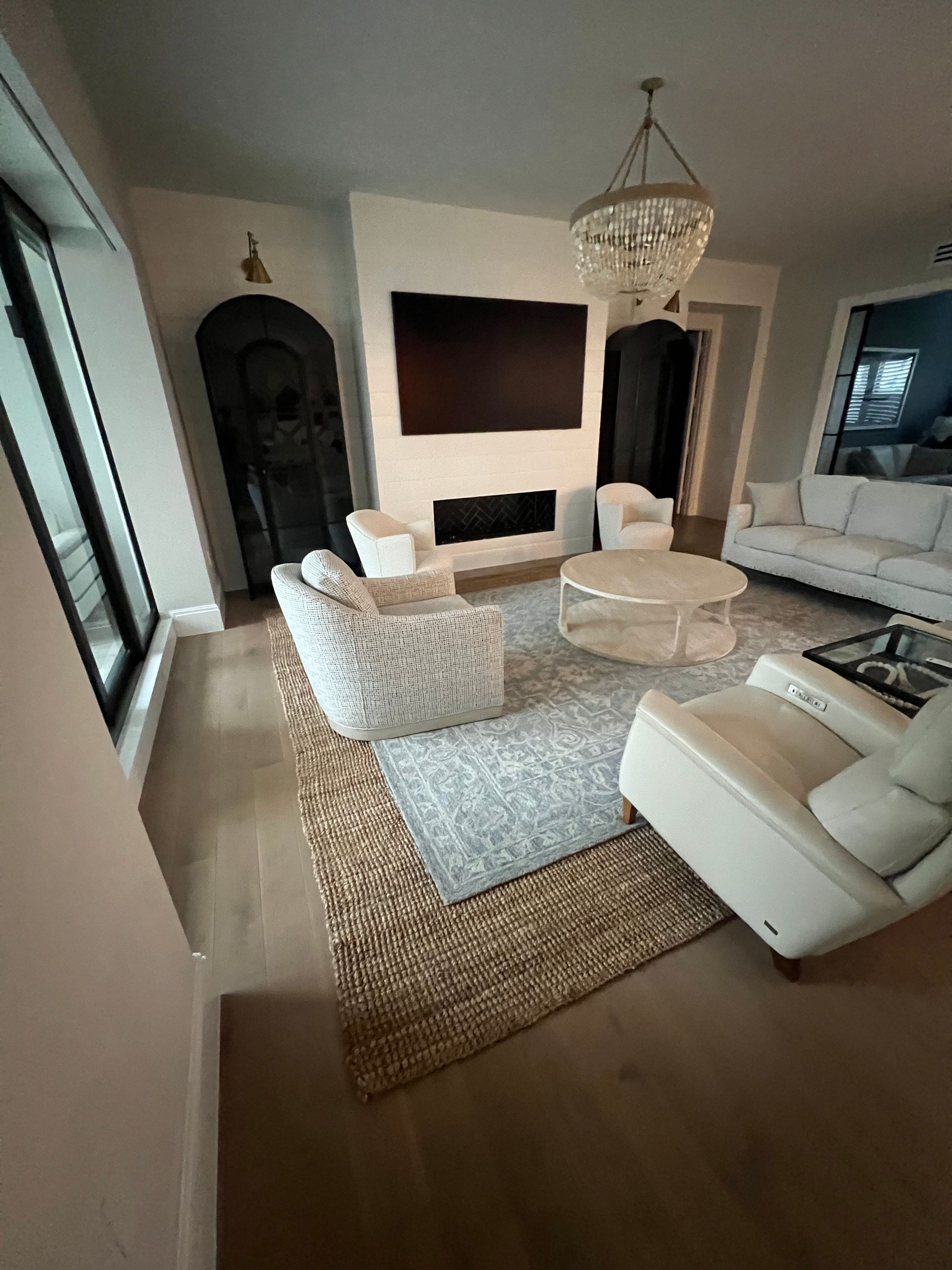 Living room with white chairs, fireplace, rug, and chandelier.