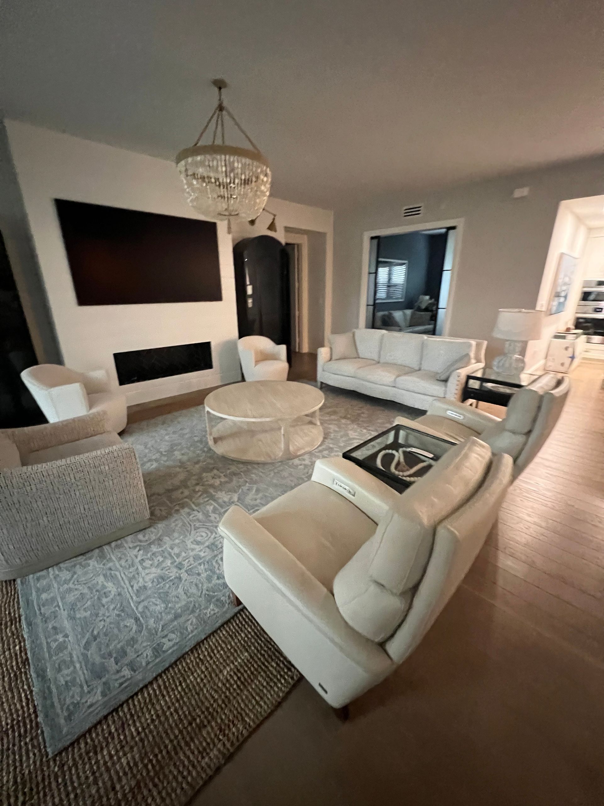 Living room with white furniture, rug, chandelier, fireplace, and large TV.