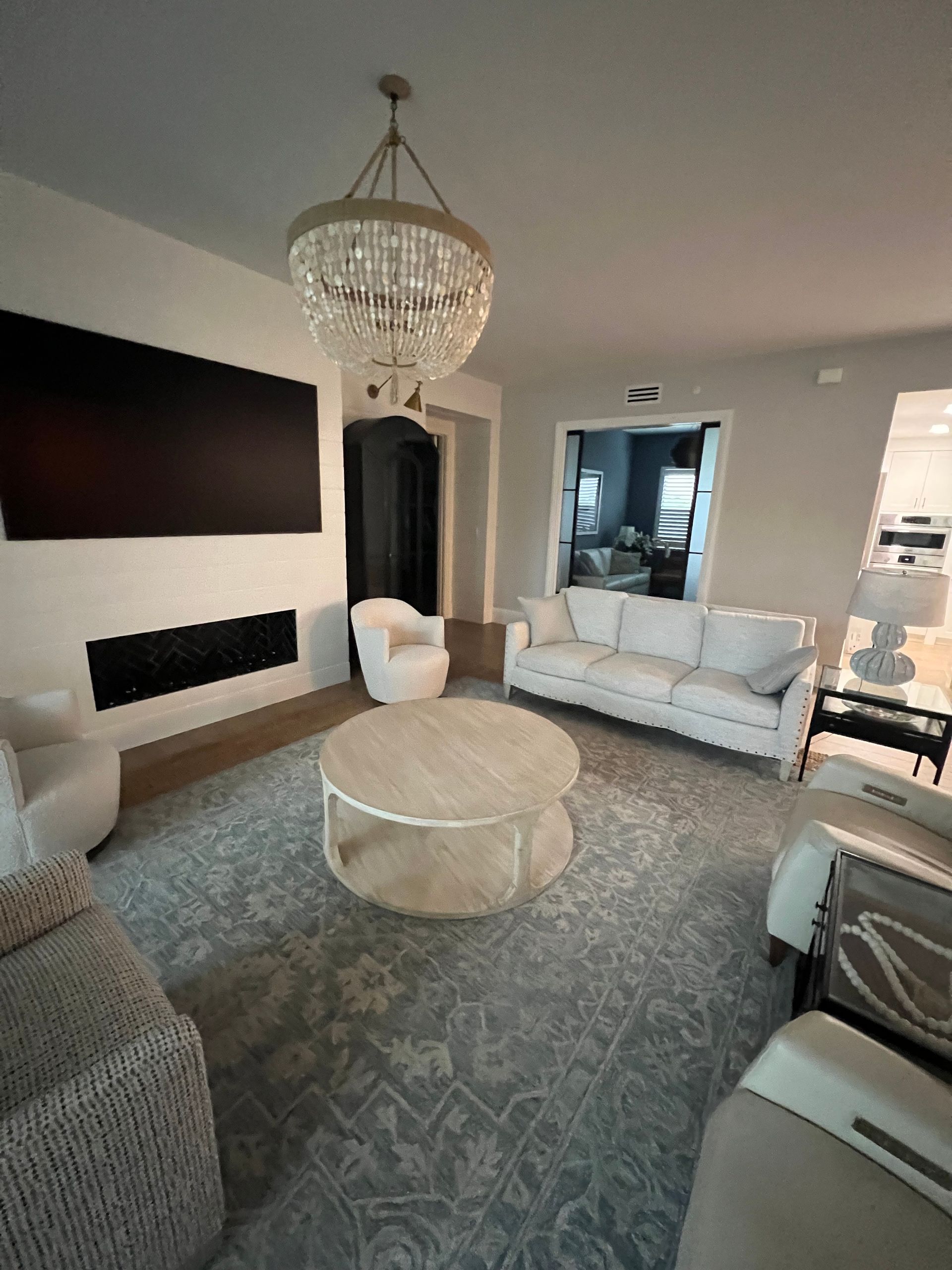 Living room with white furniture, a large rug, chandelier, and a fireplace.