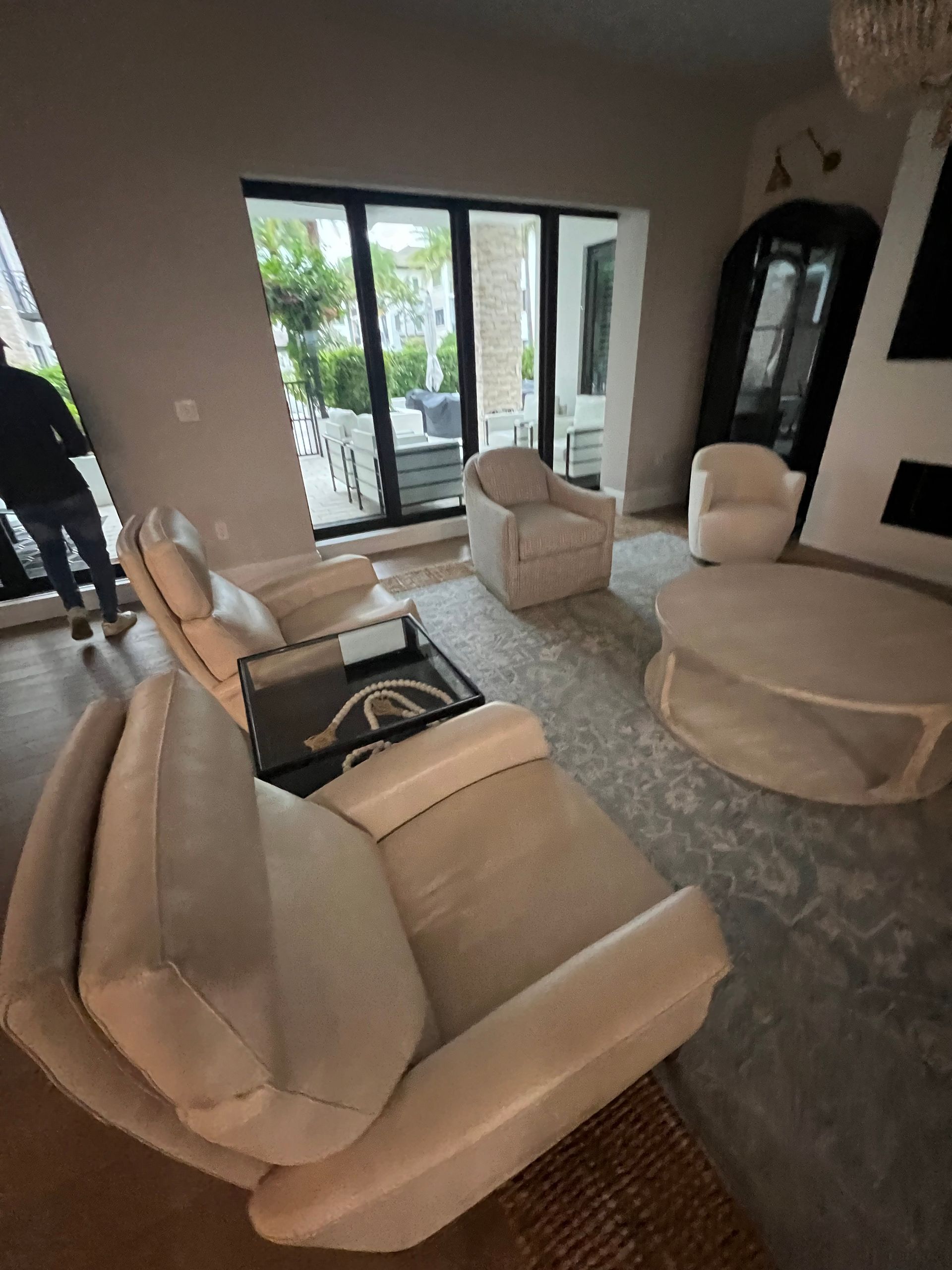 Living room with light-colored furniture, large windows, and a person standing near the doorway.
