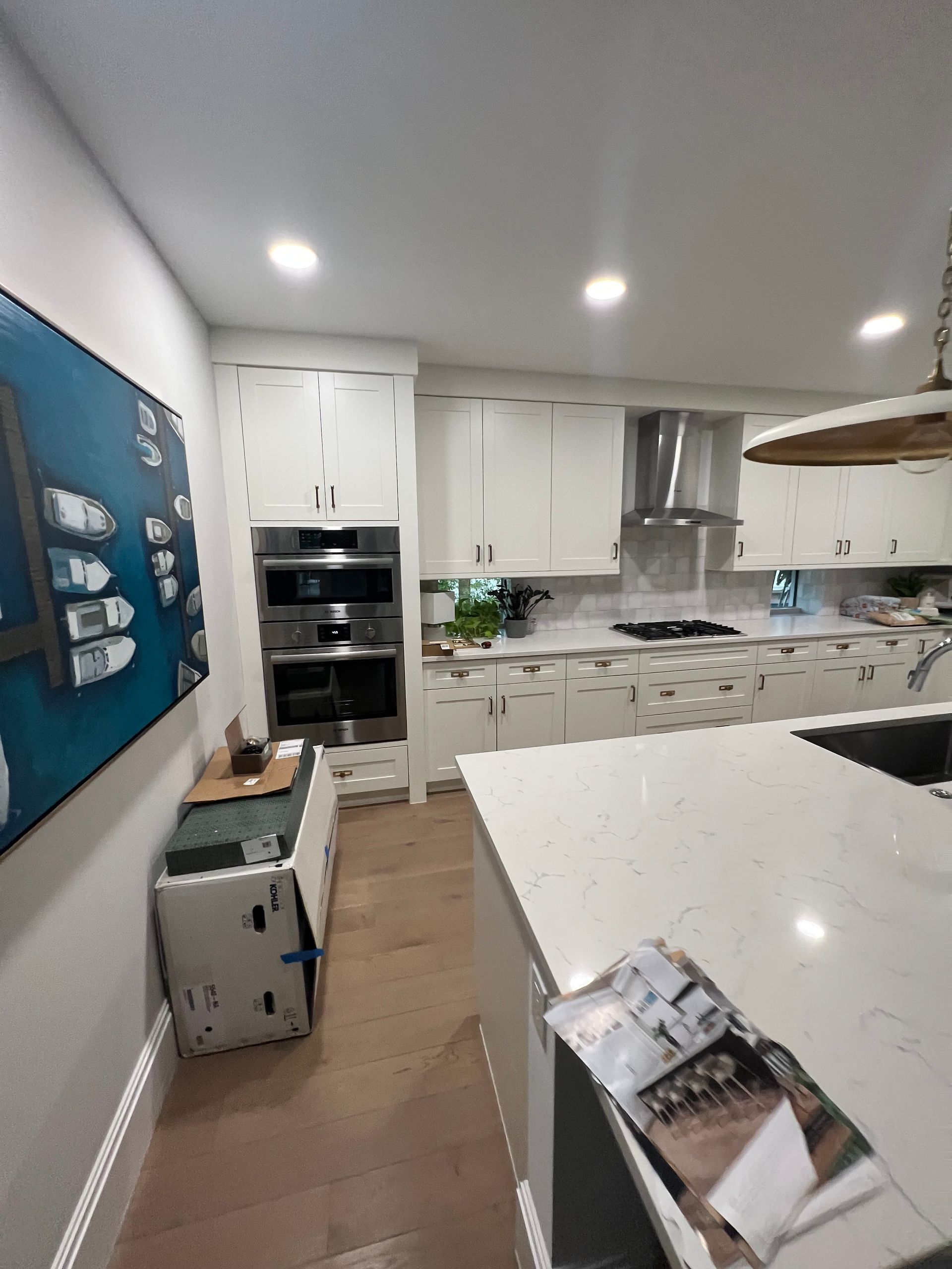 Kitchen with white cabinets, island, and appliances; partially complete. A blue boat painting on the wall.