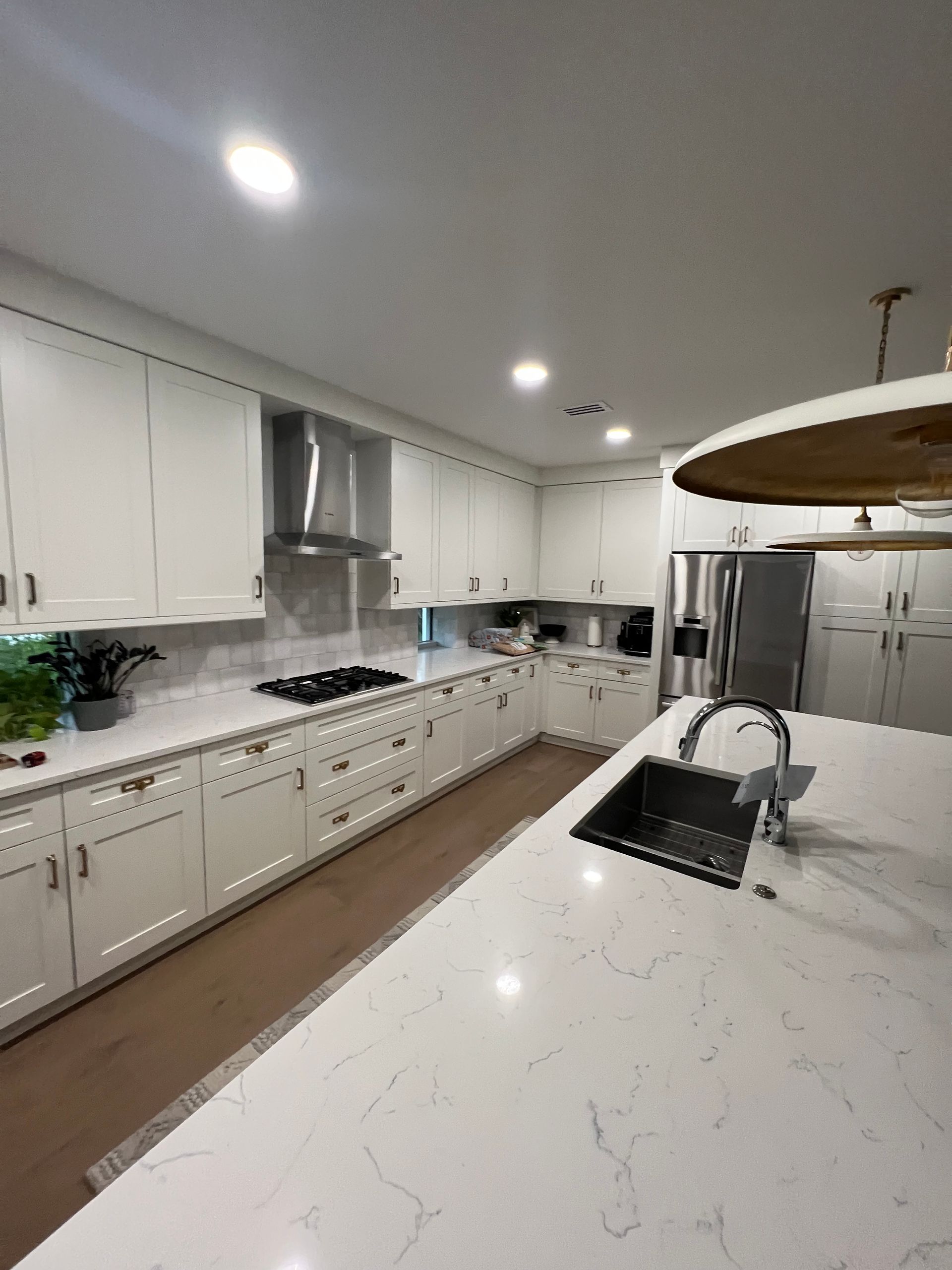 White modern kitchen with island, cabinets, stainless steel appliances and light fixtures.