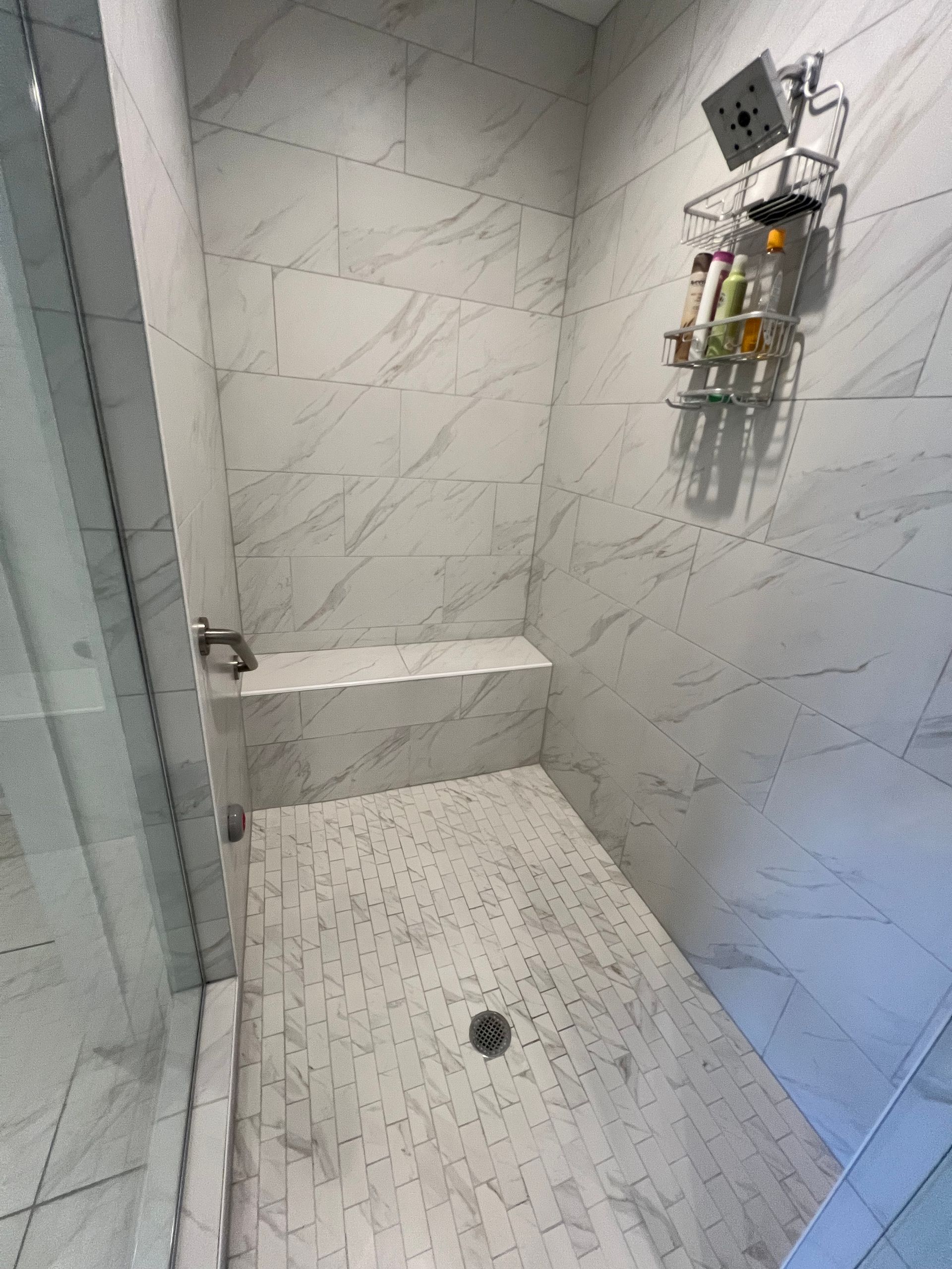 Marble-tiled shower with a built-in bench. Silver fixtures and a clear glass door.