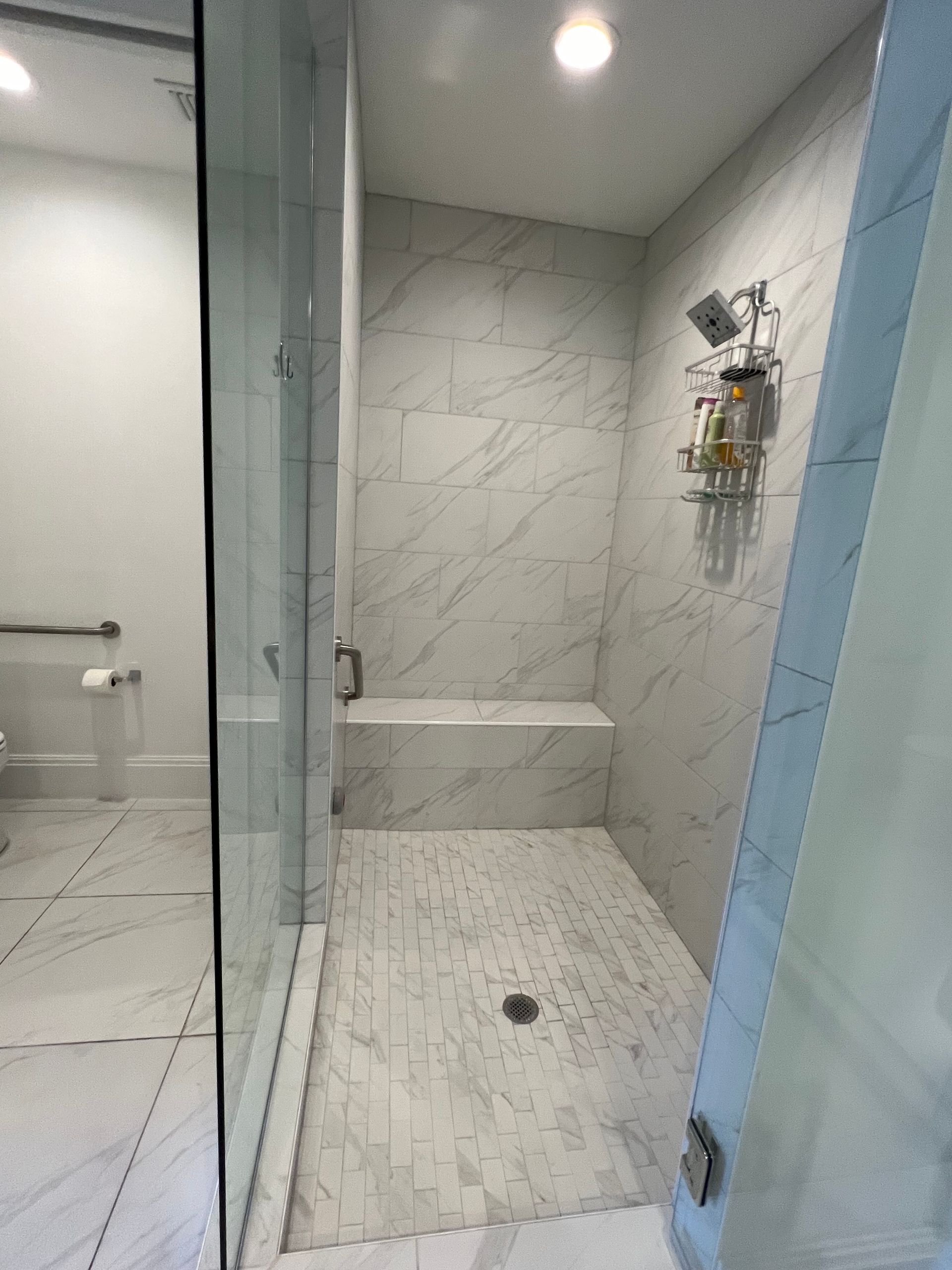 Spacious marble shower with a built-in bench and glass door.
