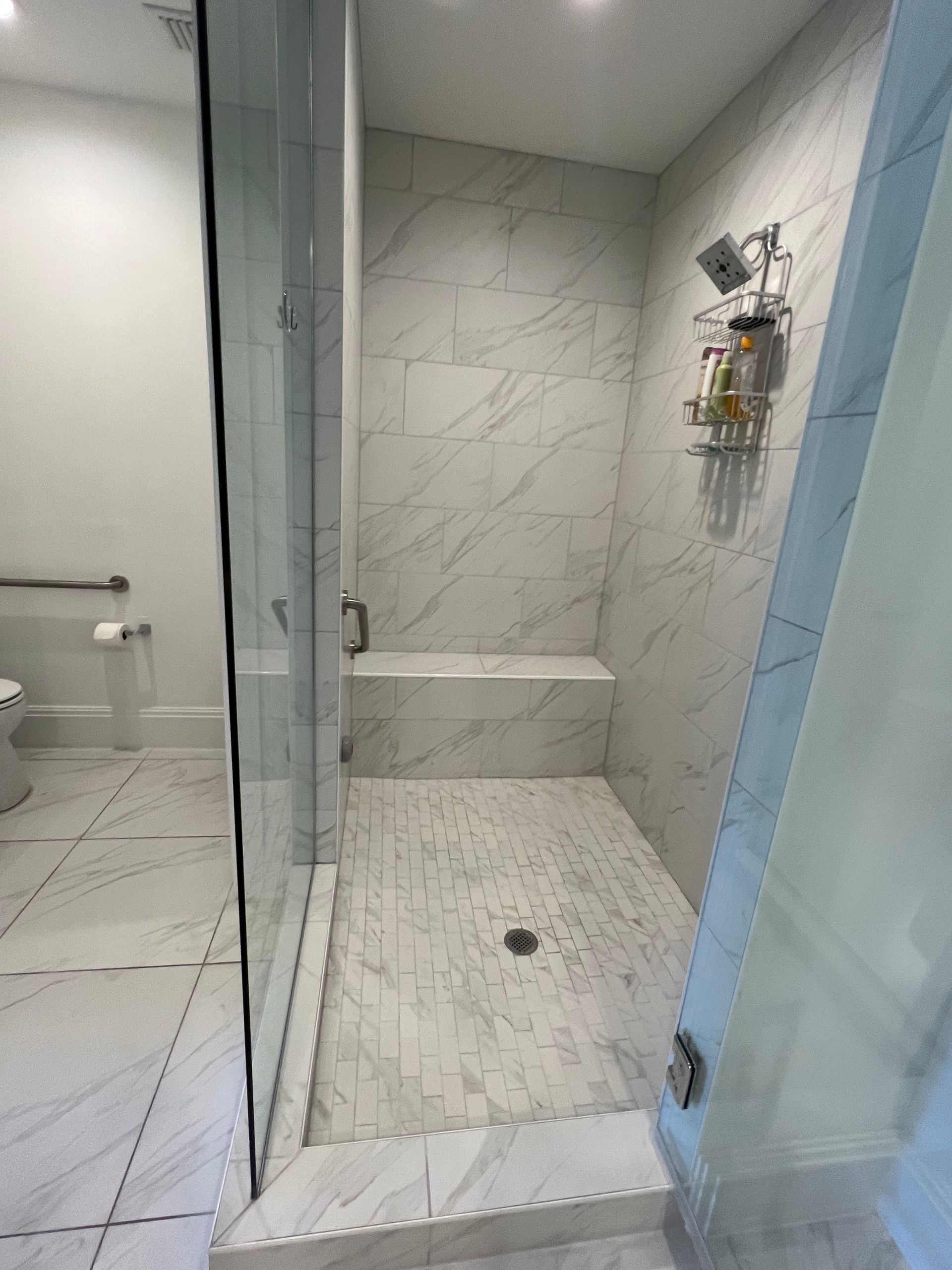 Modern bathroom with a walk-in shower featuring marble-look tiles and a built-in bench.