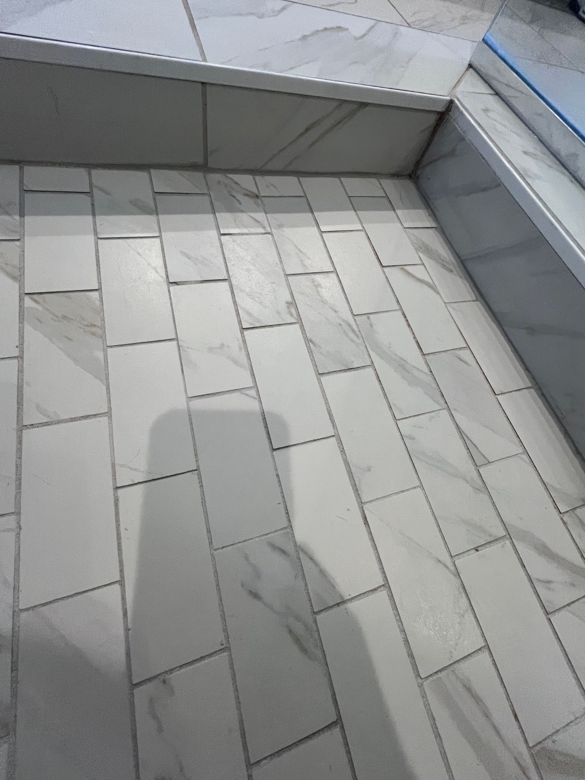 White and gray tiled shower floor, with rectangular tiles in a brick pattern.