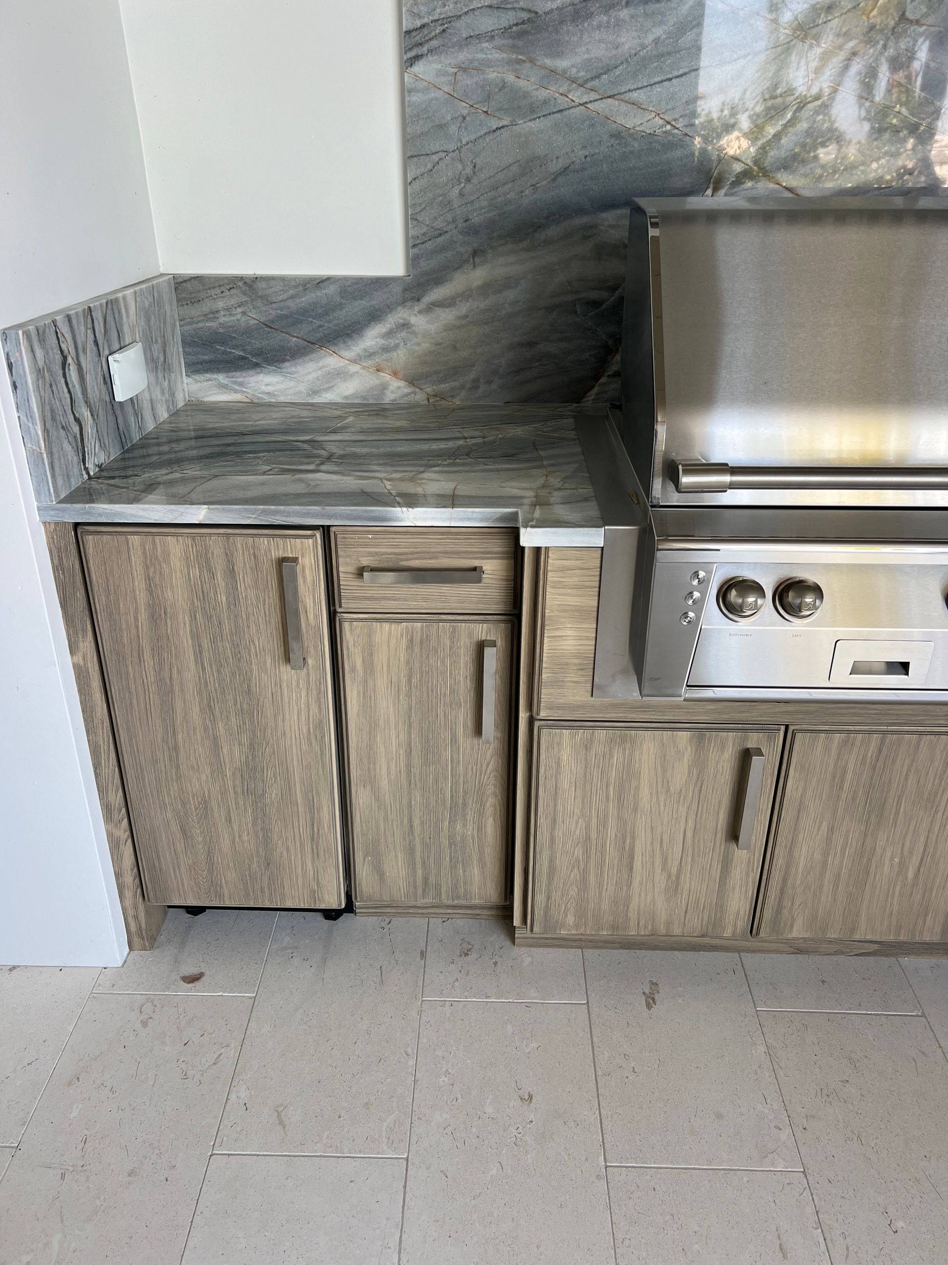 Outdoor kitchen with gray and brown cabinets, granite countertop, stainless steel grill.