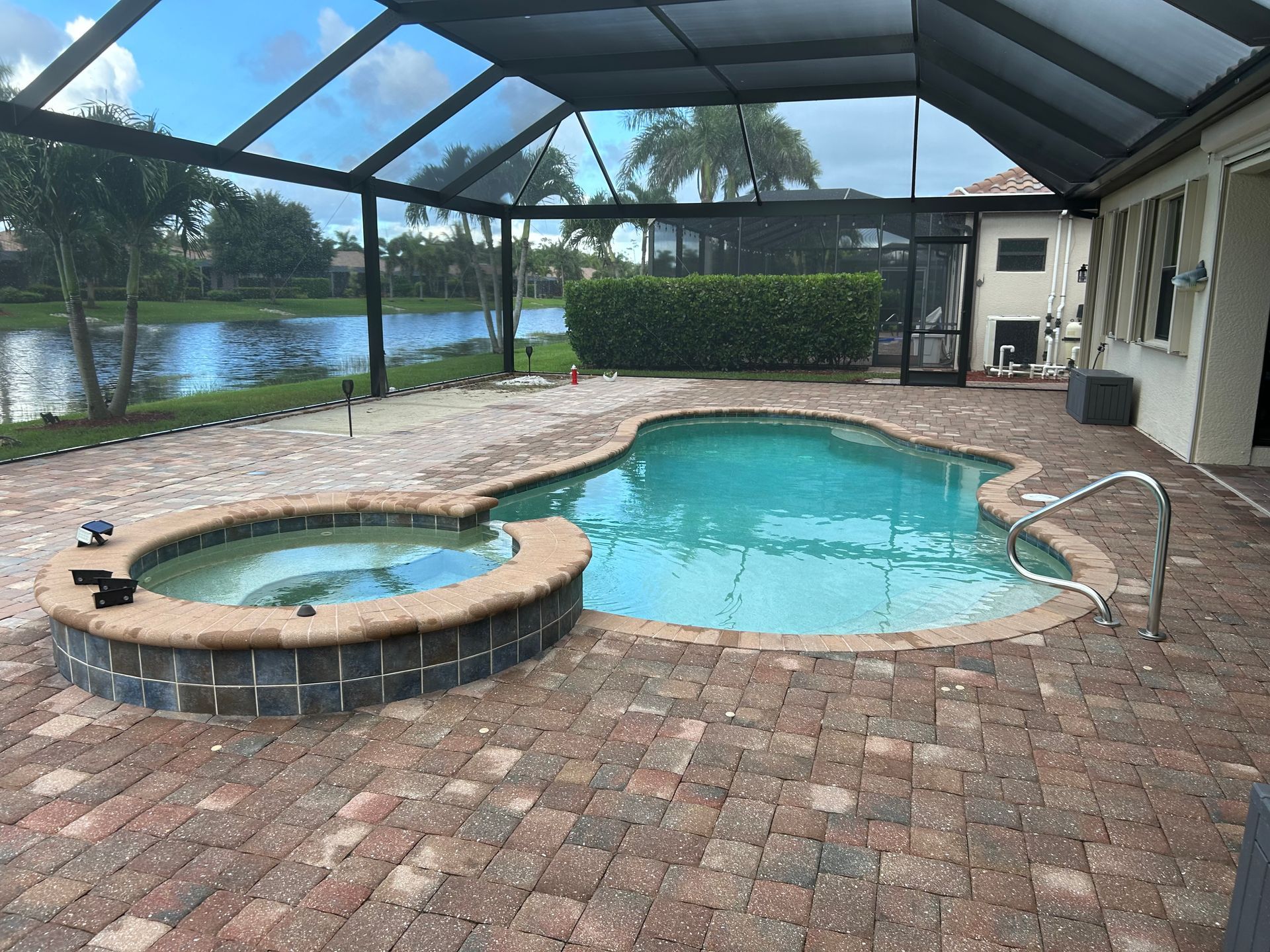 Pool and spa surrounded by brick patio, under a screened enclosure. Exterior shot with lake view.
