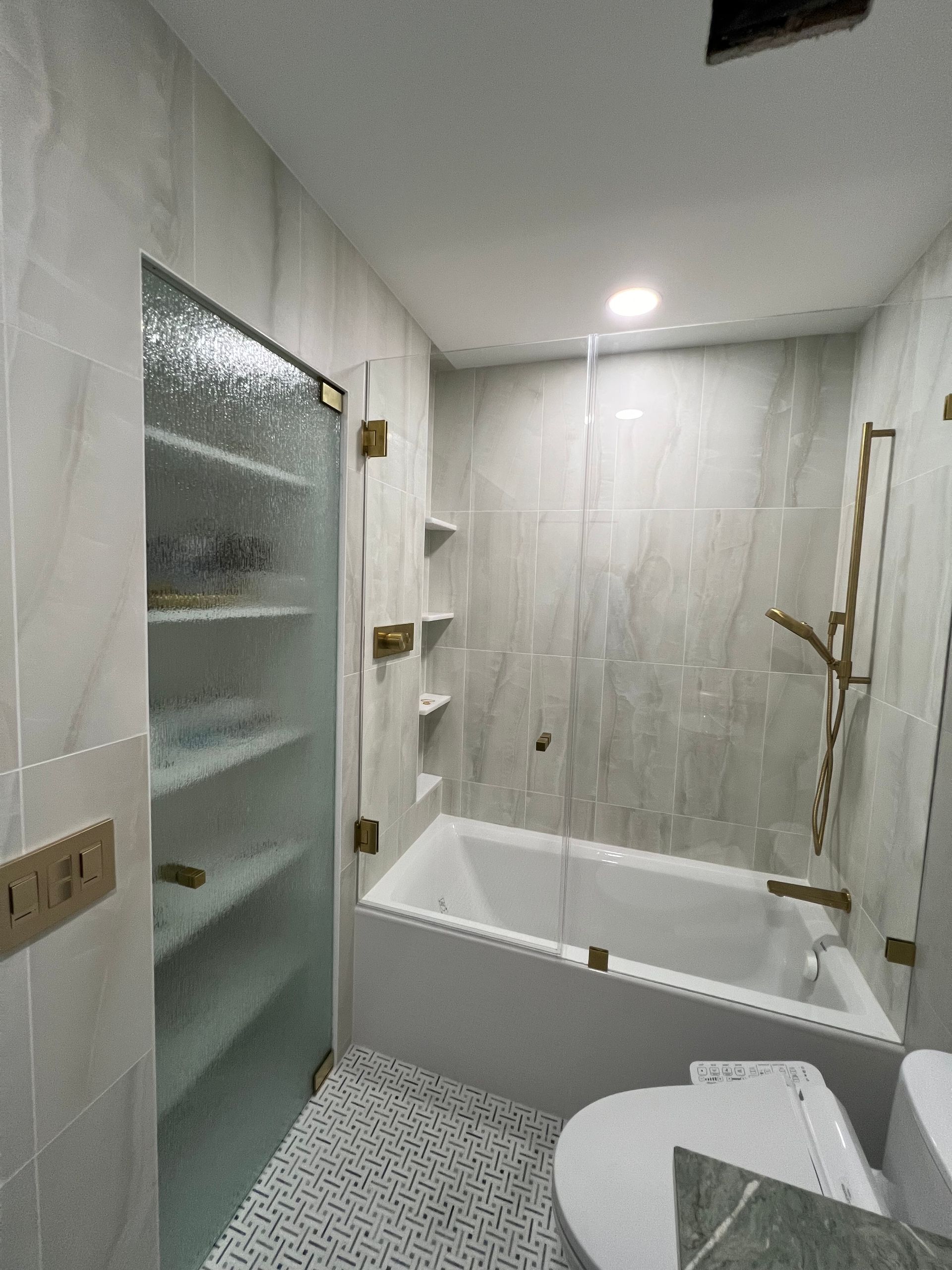 Bathroom with white and gray tile, a bathtub, and a glass shower door.
