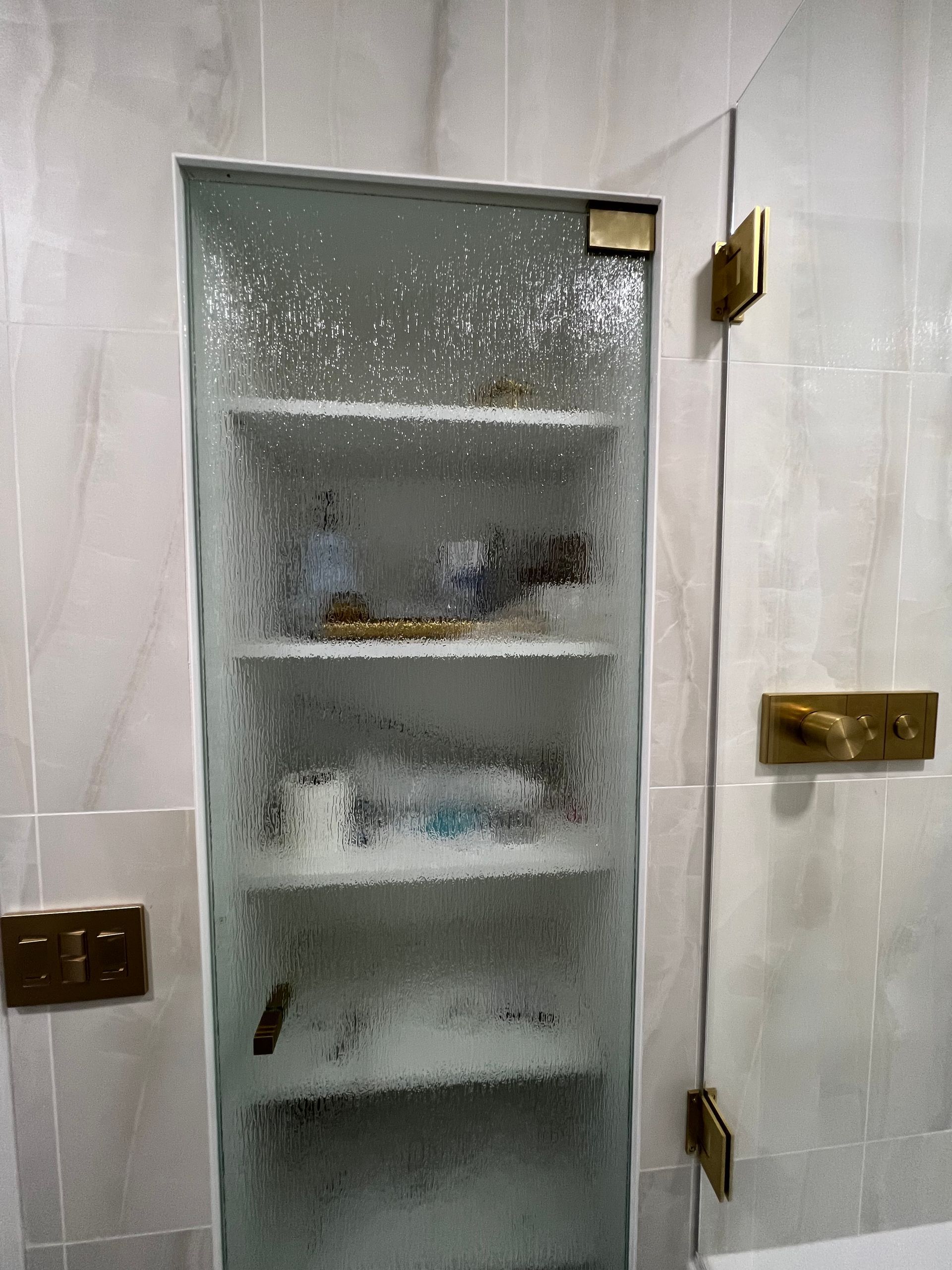 Bathroom cabinet with frosted glass door, brass hinges and hardware, against tiled wall.