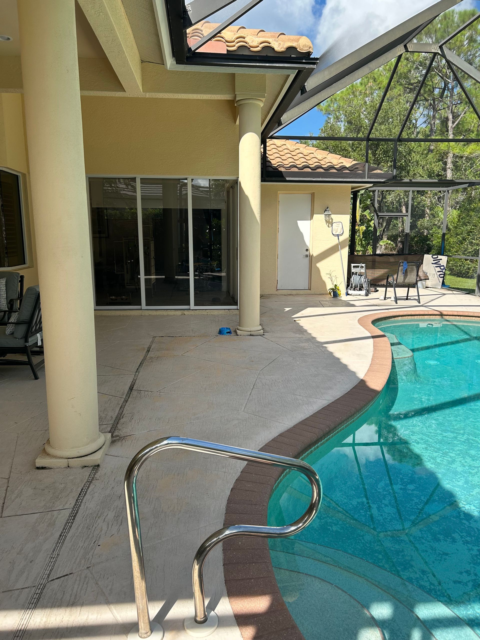 Poolside view with pool, handrail, beige columns, and sliding glass doors.