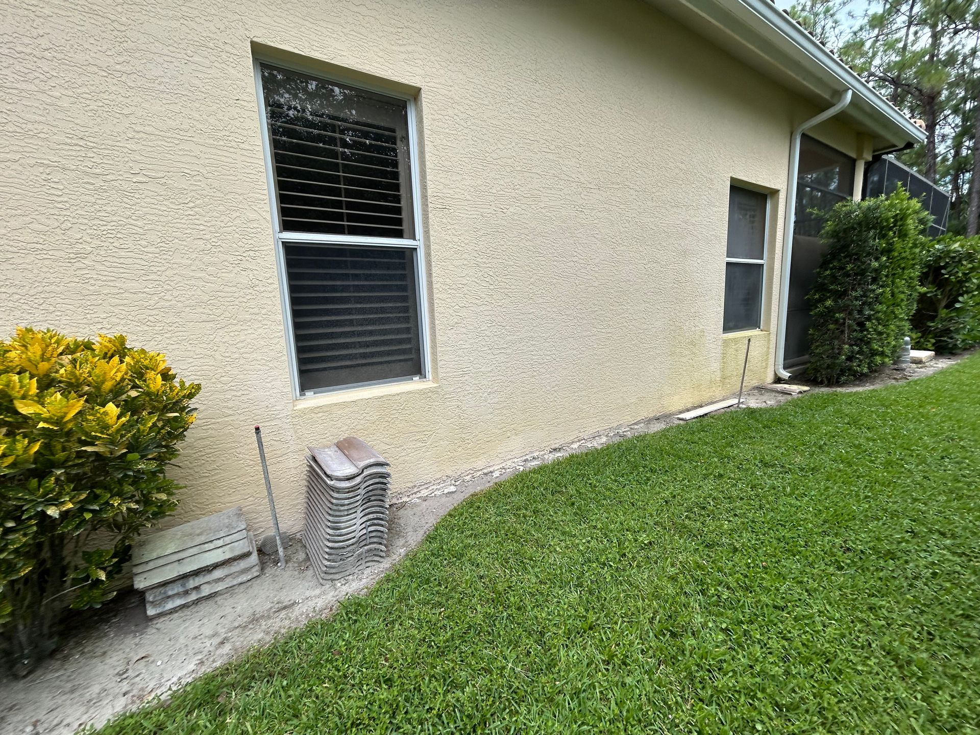 Beige stucco house exterior with window, door, and lawn. Green grass and bushes.