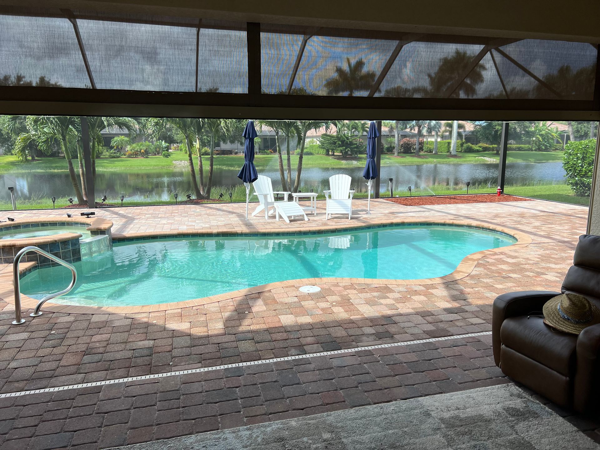 A pool with a spa, white chairs, and a lake view, framed by a screened patio.