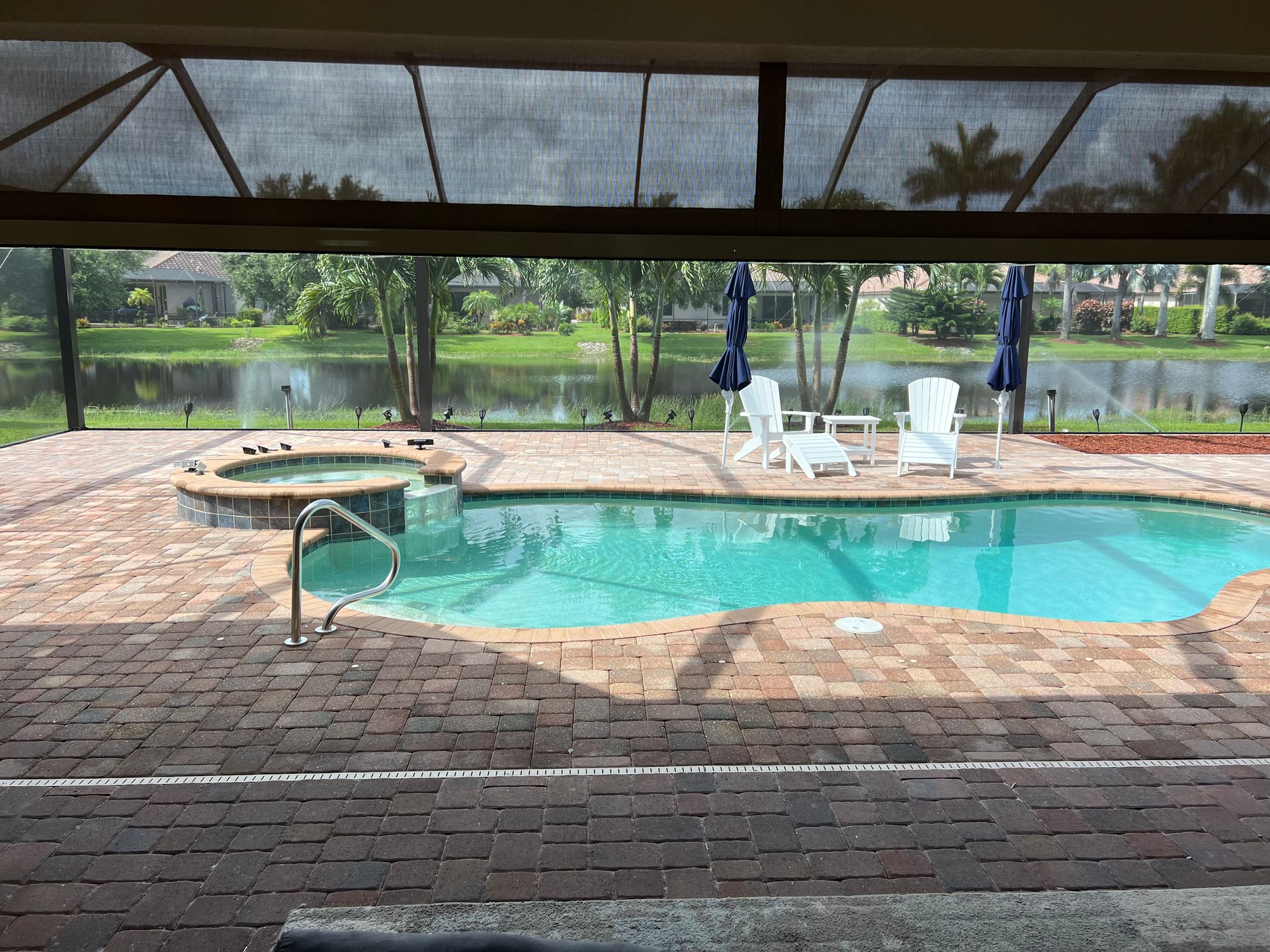 Pool area with a pool, hot tub, white chairs, and a lake view.