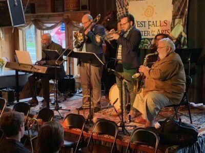 Jazz band performing onstage at West Falls Center for the Arts; musicians with instruments, audience in foreground.