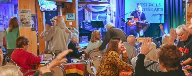 People at a bar, watching a musician on stage playing a guitar.