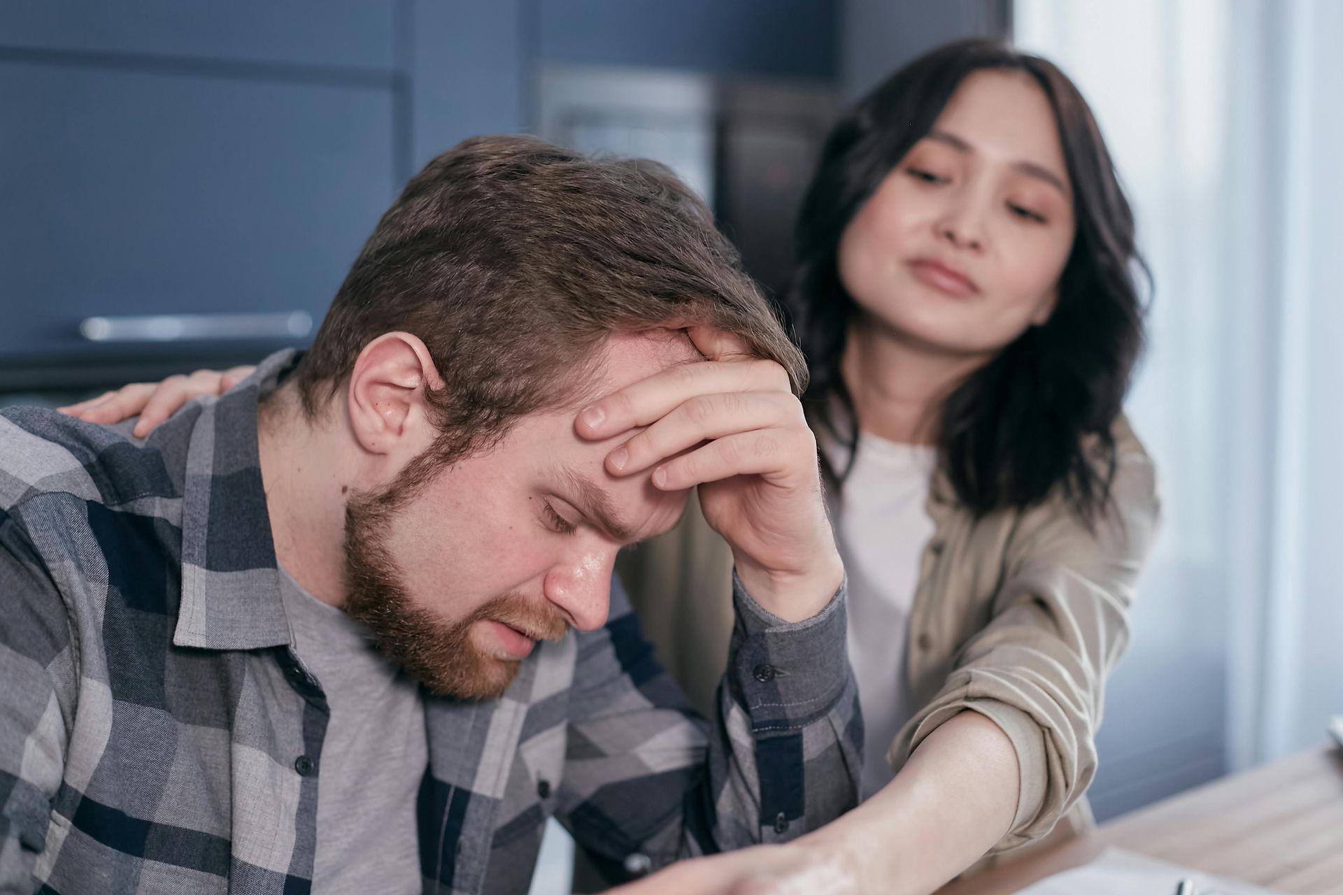 Man holding his head while a woman comforts him at a table with documents — header for 